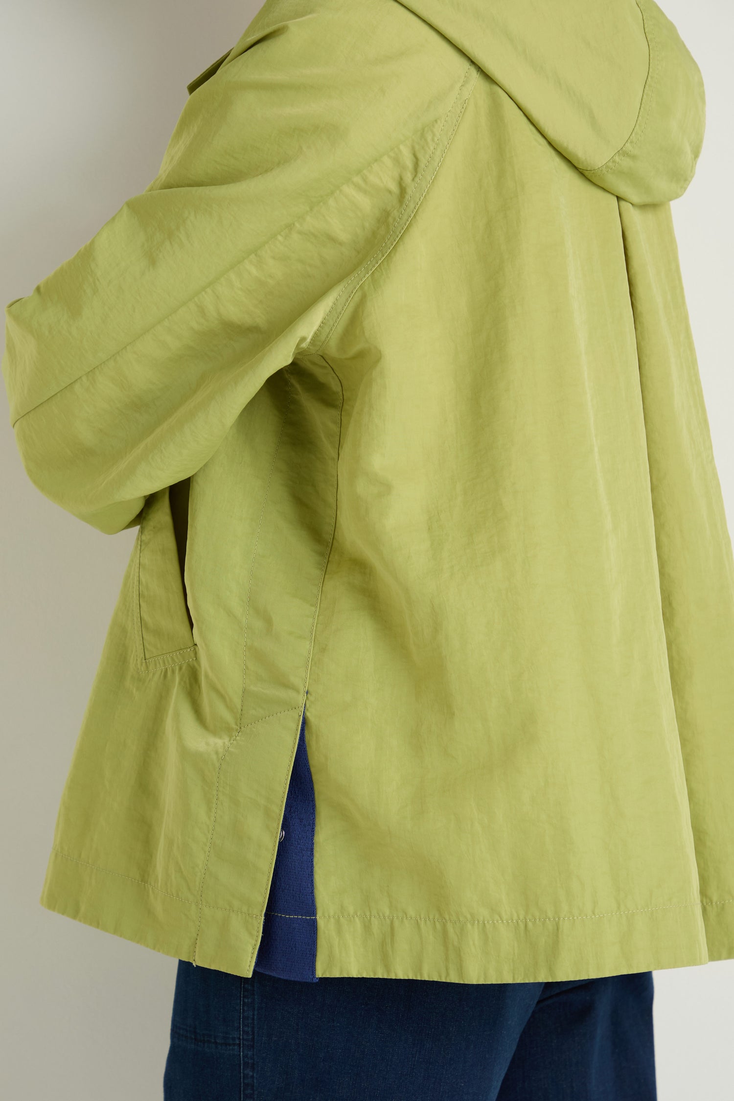 A person shown from the back and side wears a light green Showerproof Boxy Rain Jacket with dark blue pants against a plain background.
