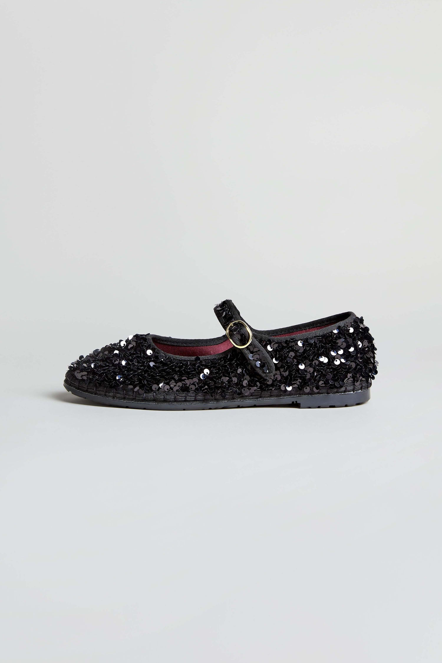 The Sequin Mary Jane Shoes, handmade in Spain, feature black sequins and a buckle strap, and are displayed on a plain light background.