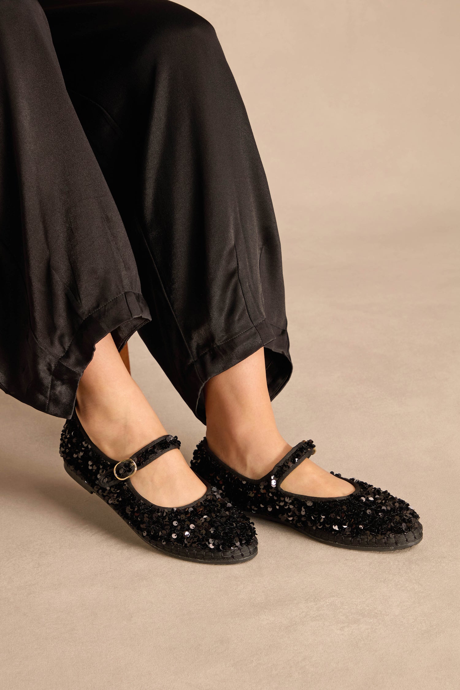 Black sequined Sequin Mary Jane Shoes with an ankle strap worn with black trousers.