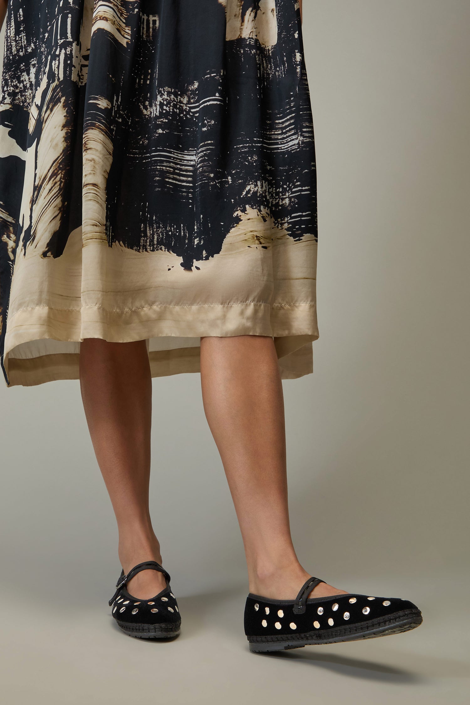 A person wearing a black and beige patterned skirt and chic Studded Mary Jane Velvet Shoes stands against a plain background.