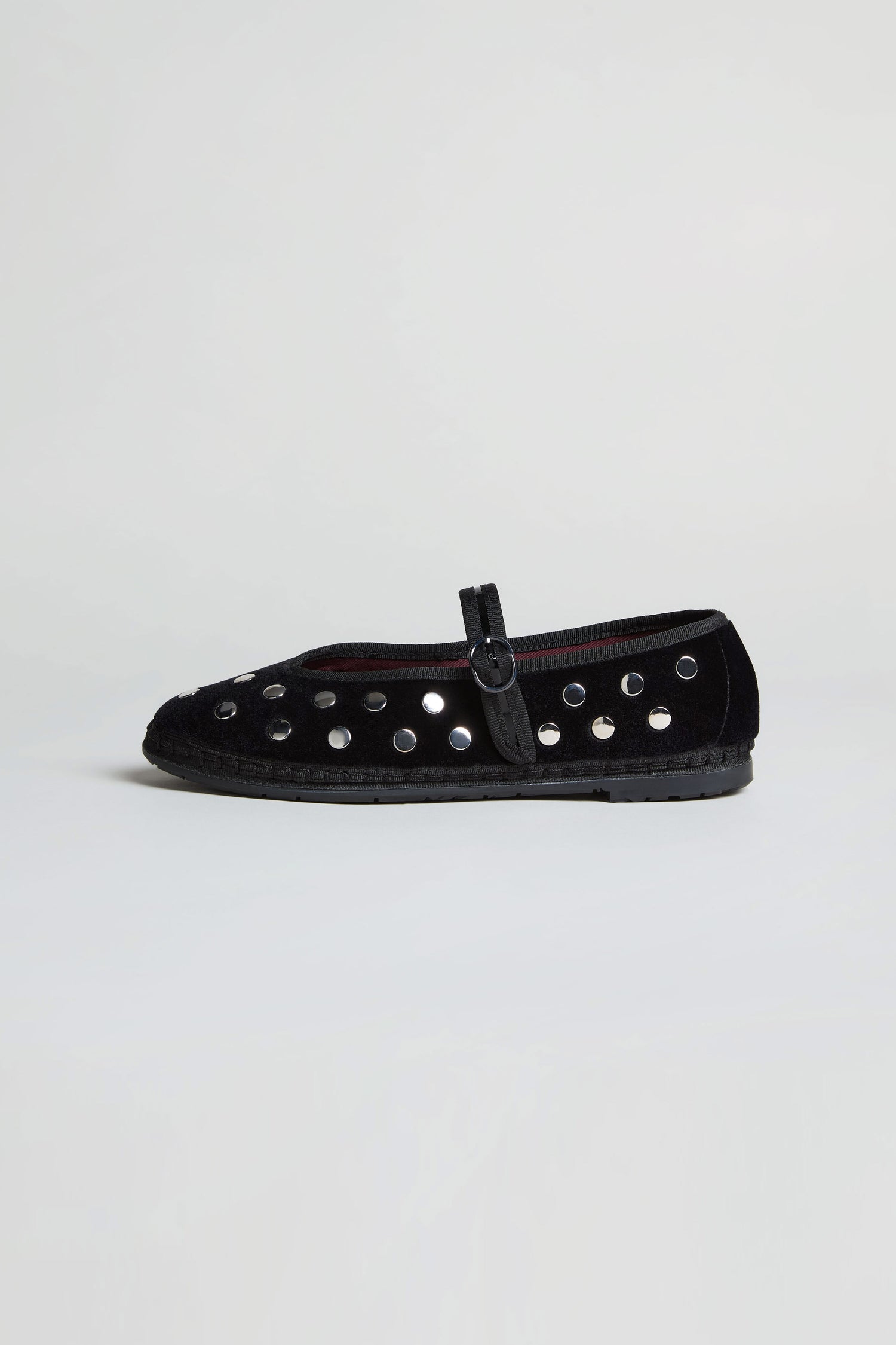 The Studded Mary Jane Velvet Shoes feature black velvet, a buckle strap, and multiple silver eyelets along the sides, exemplifying elegant handmade Spanish footwear against a plain white background.