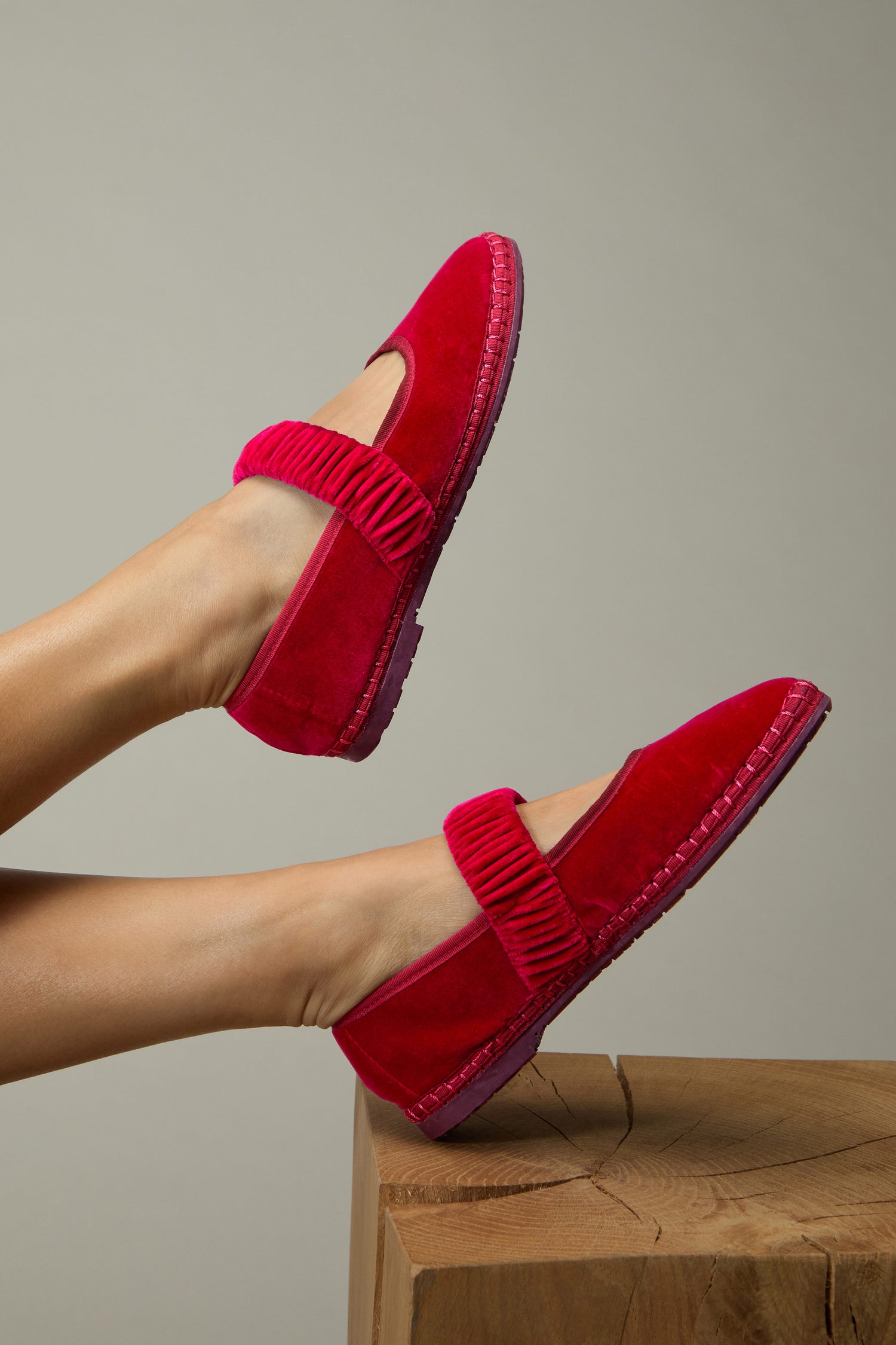 A person wearing Mafalda Fuchsia Velvet Shoes with textured straps and a recycled rubber sole rests their feet on a wooden block against a plain background.