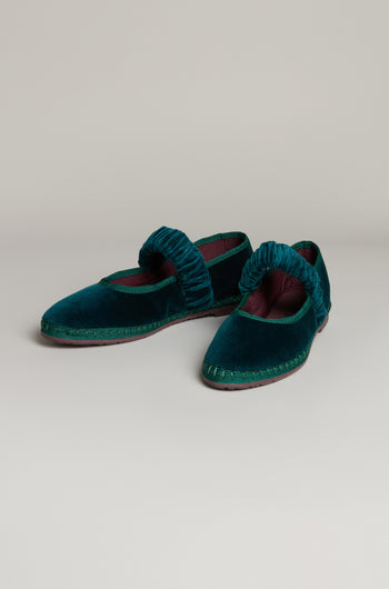 The Mafalda Teal Velvet Shoes feature ruched straps, a dark maroon lining, and a recycled rubber sole. Handmade in Spain from velvet, this flat pair is shown against a neutral background.