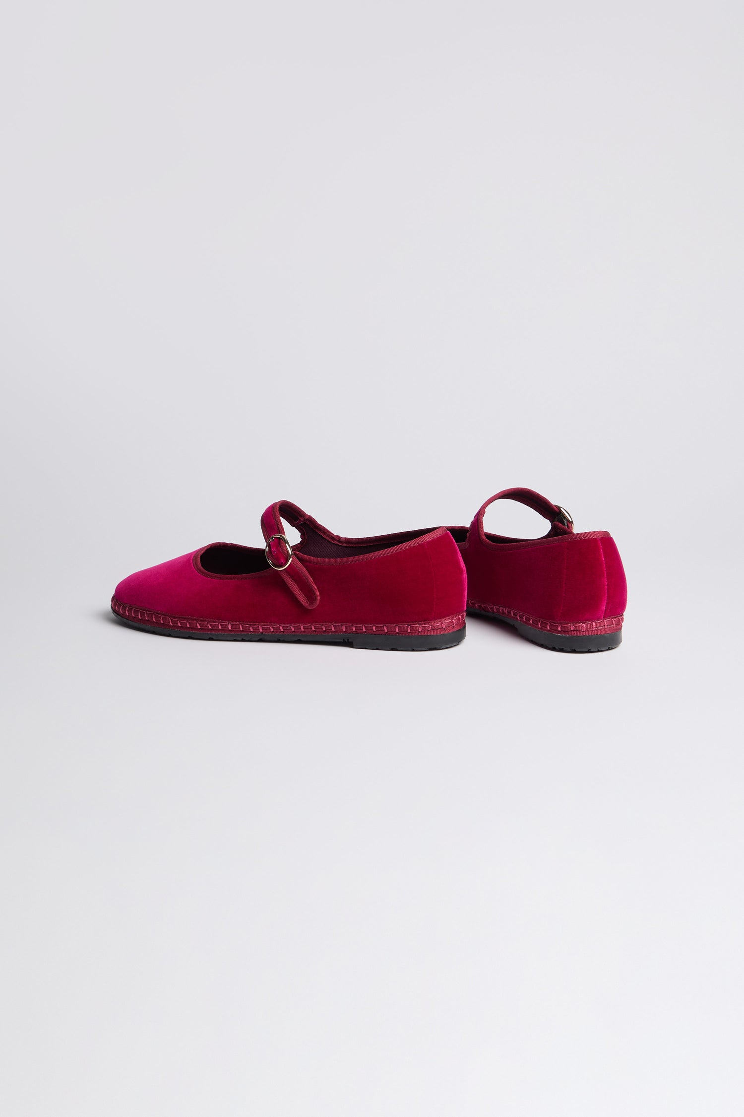 A pair of Fuchsia Mary Jane Velvet Shoes with black soles, one facing forward and the other turned to the side, displayed on a plain light background—showcasing vintage charm and timeless elegance.