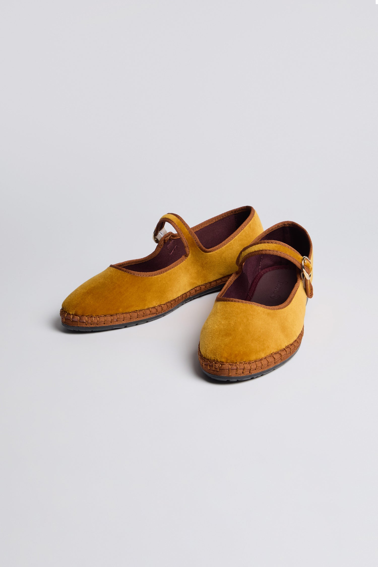 Mustard Mary Jane Velvet Shoes feature brown straps and stitching details, crafted sustainably in mustard yellow velvet, displayed on a plain light background.