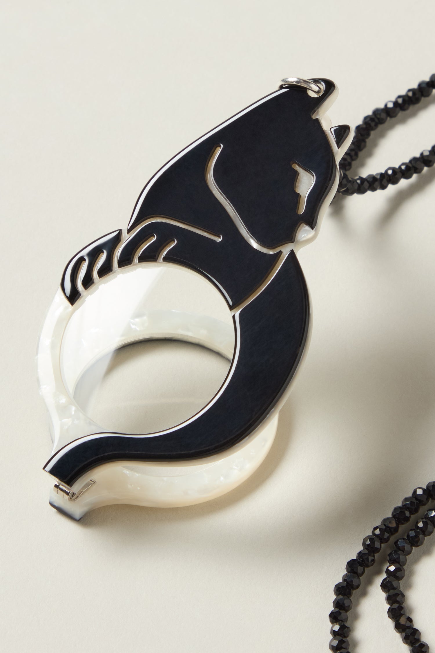 Cat Pendant Glasses feature a pendant shaped like a stylized black cat on a circular white base, hanging from a black beaded chain. Optical-grade craftsmanship ensures a sophisticated and elegant accessory.