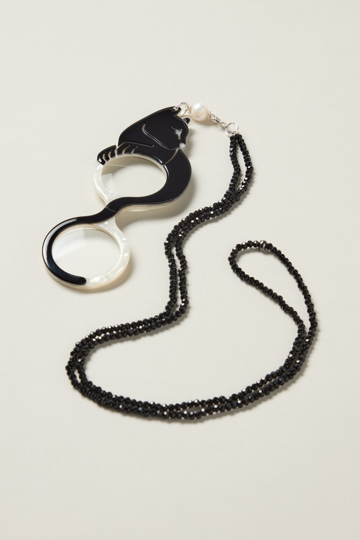 Cat Pendant Glasses feature optical-grade craftsmanship, a pearl detail, and hang from a black beaded chain, shown on a neutral surface.