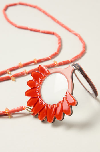 The Daisy Pendant Glasses, featuring a red daisy magnifying lens and matching beaded chain, are displayed on a neutral background.