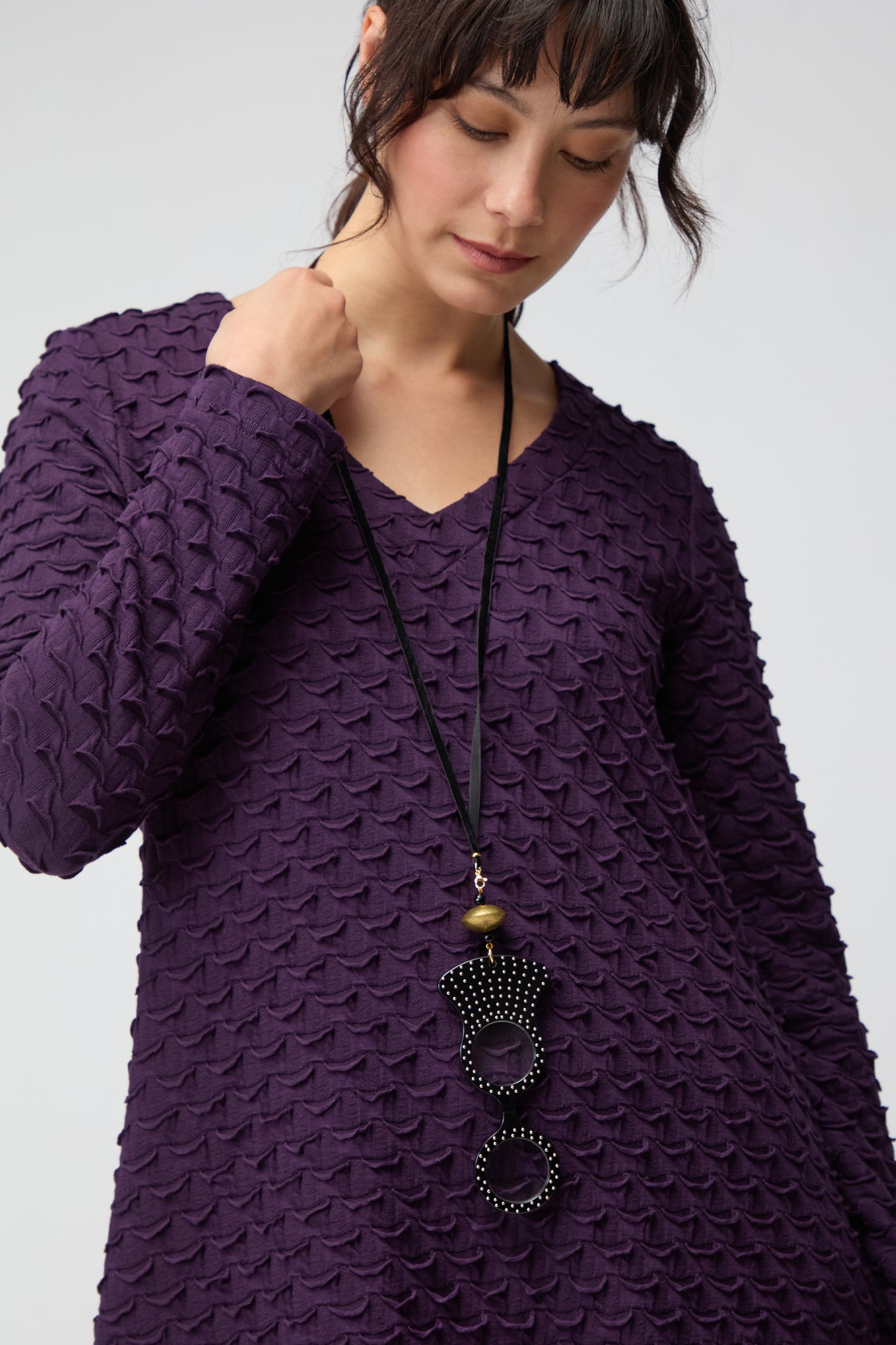 A woman wearing a textured purple long-sleeve top and the handmade in Spain Rock and Roll Pendant Glasses necklace with large circular beaded pendants looks down.