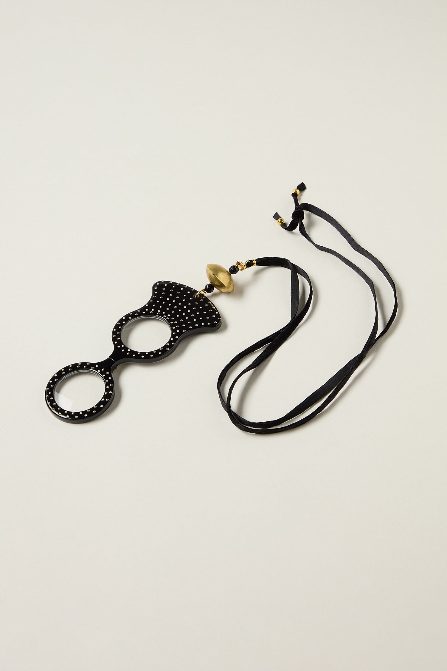 Introducing the Rock and Roll Pendant Glasses: black and gold eyewear with two lenses, adorned with small studs and attached to a long black ribbon—handmade in Spain for a stylish statement.