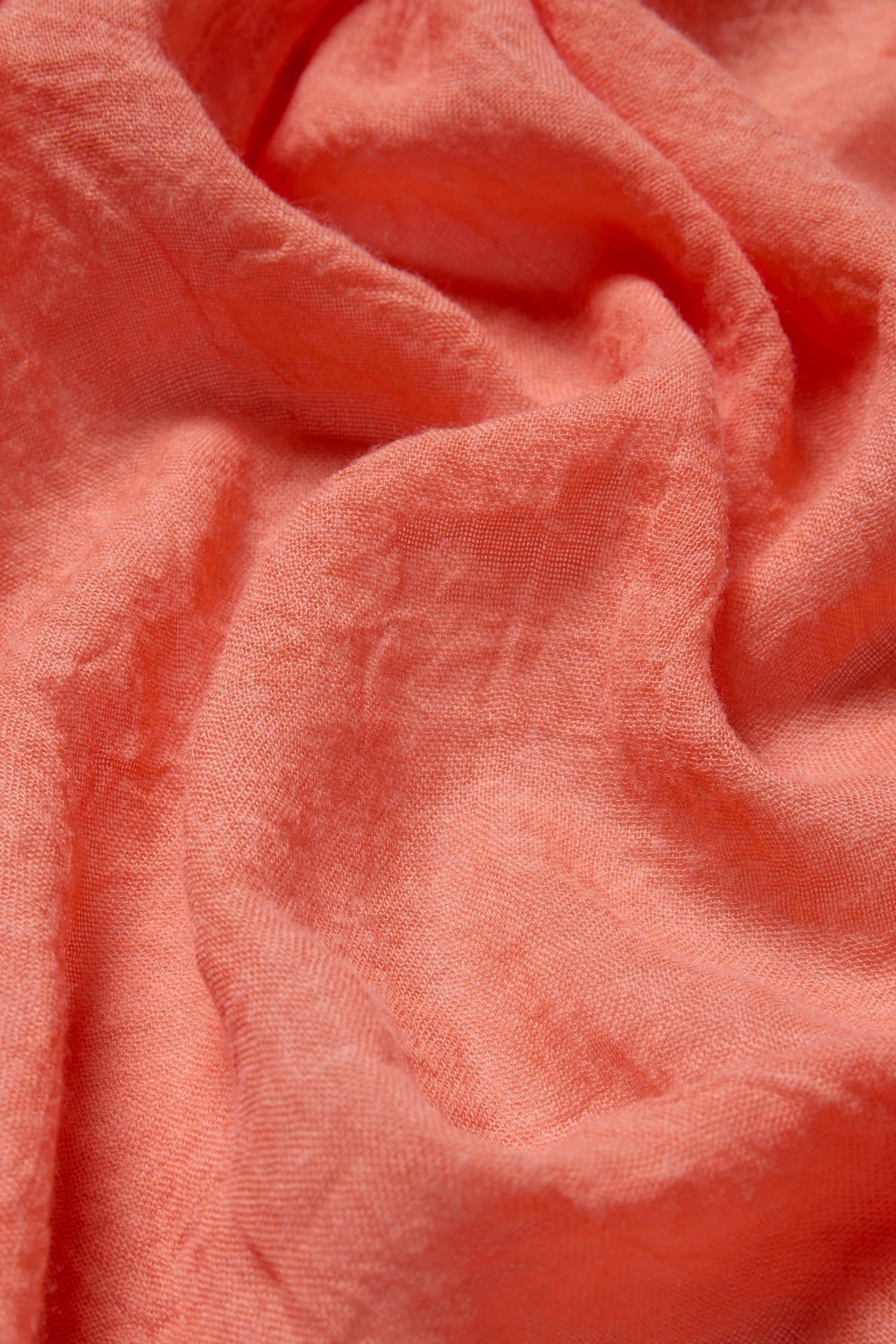 Close-up of the Soft Fringe Scarf in coral, featuring its textured material, subtle creases, and soft fringe detailing.