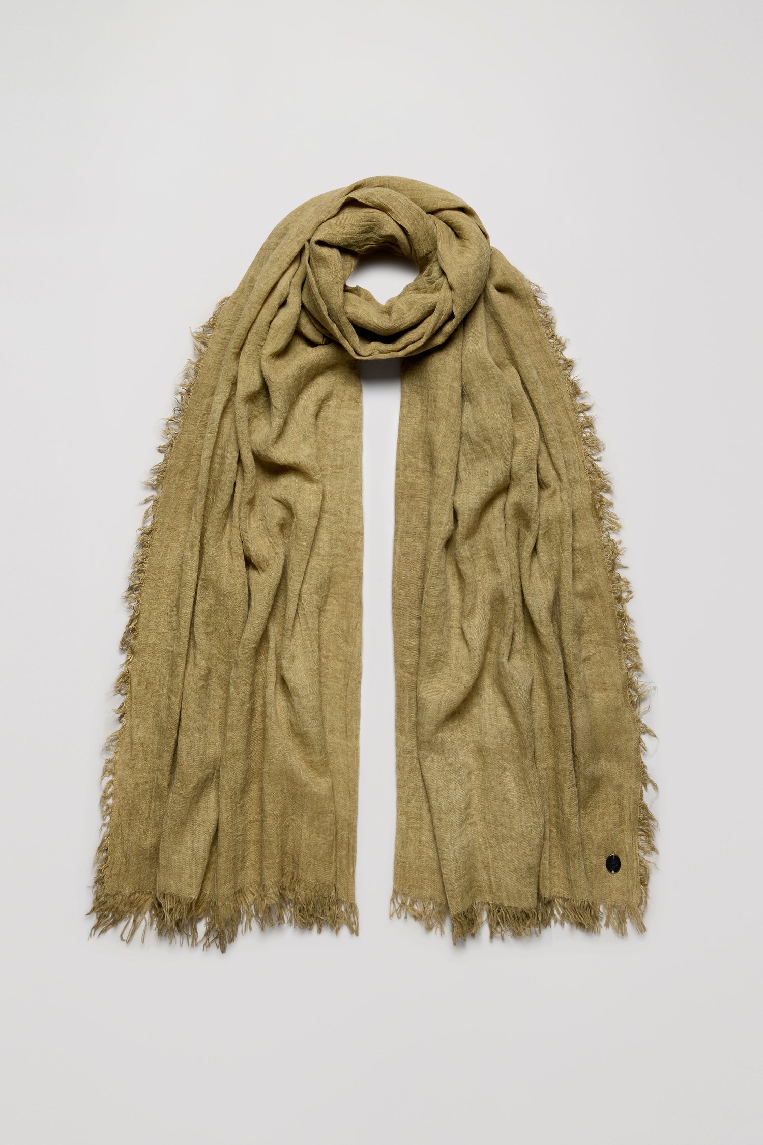 The Soft Fringe Scarf features a light brown textured material with soft frayed edges and is shown laid flat on a plain light background, offering versatile styling options.
