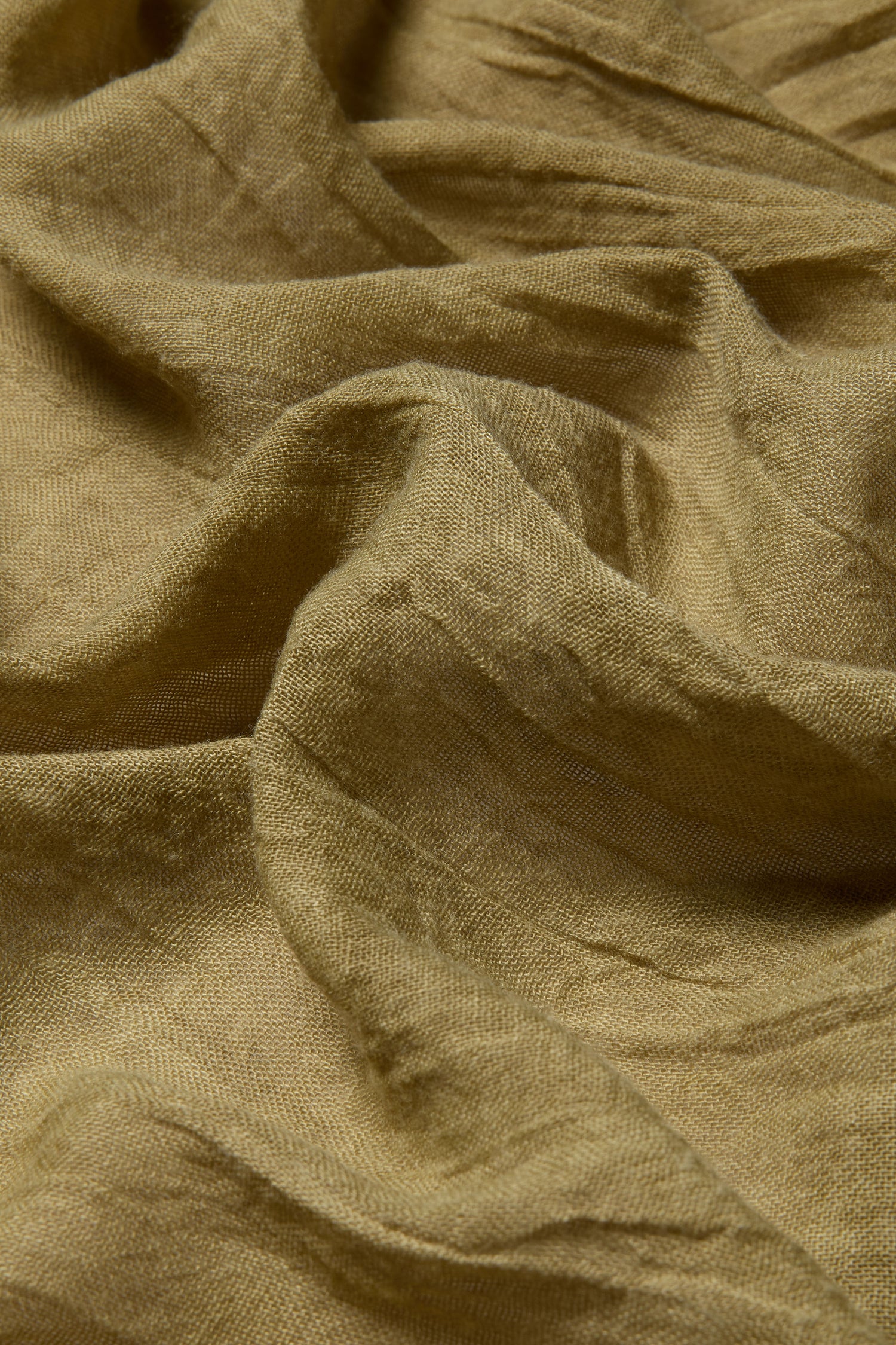 Close-up of olive green textured material with natural folds highlights the versatile styling options of the Soft Fringe Scarf.