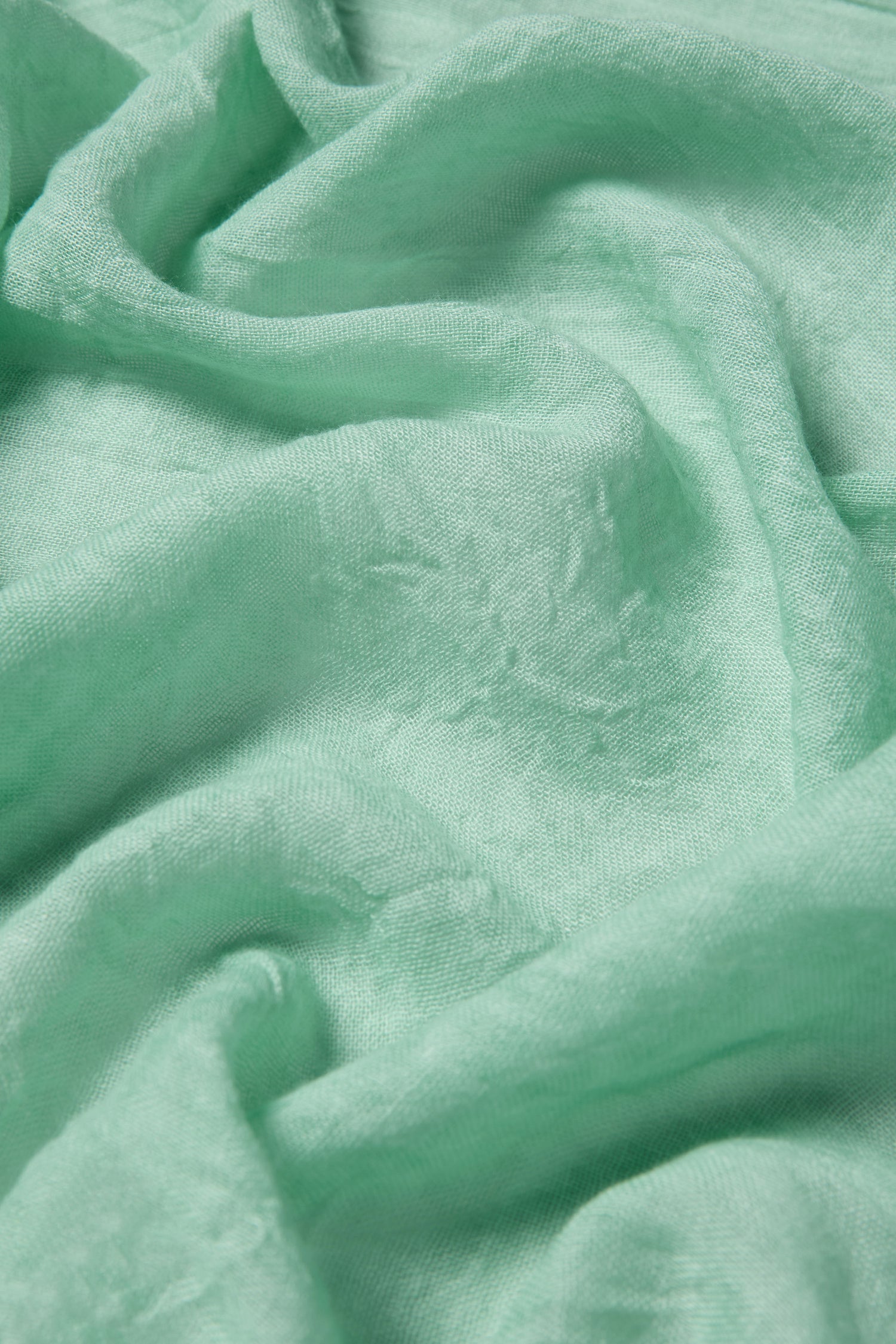 Close-up of the Soft Fringe Scarf in light mint green, highlighting its soft, subtly wrinkled texture and gentle sheen for versatile styling.