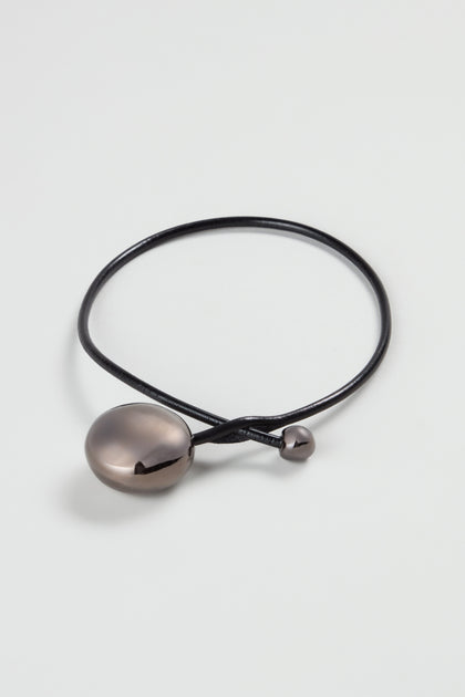 The Charcoal Handmade Ceramic Bead Necklace features a black cord with a large oval ceramic pendant and a small round bead, artisanal in style and inspired by French design, displayed on a plain white background.