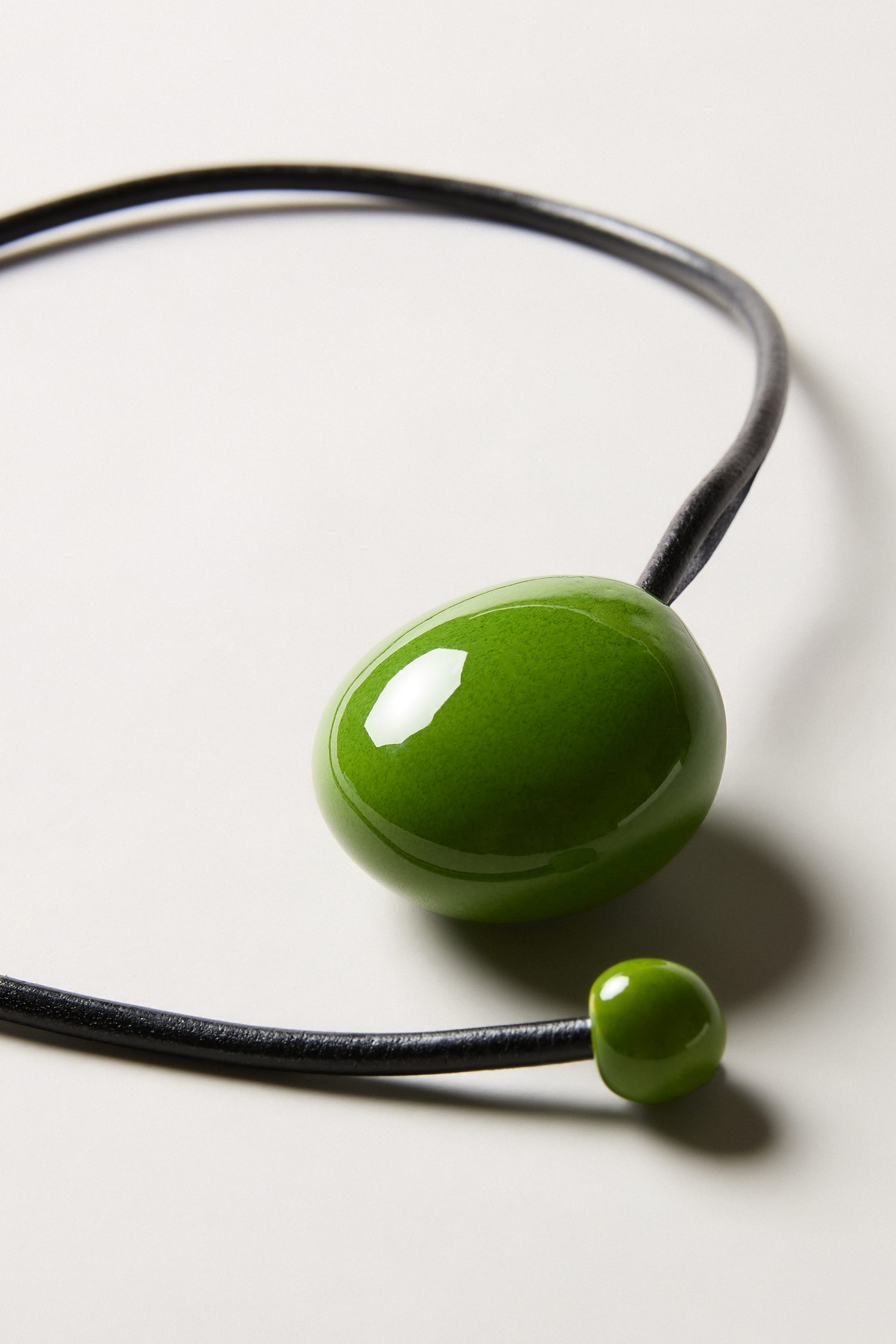 The Moss Handmade Ceramic Bead Necklace features a black cord with two glossy green ceramic beads—one large, one small—handmade and displayed on a light background for a striking artisan look.