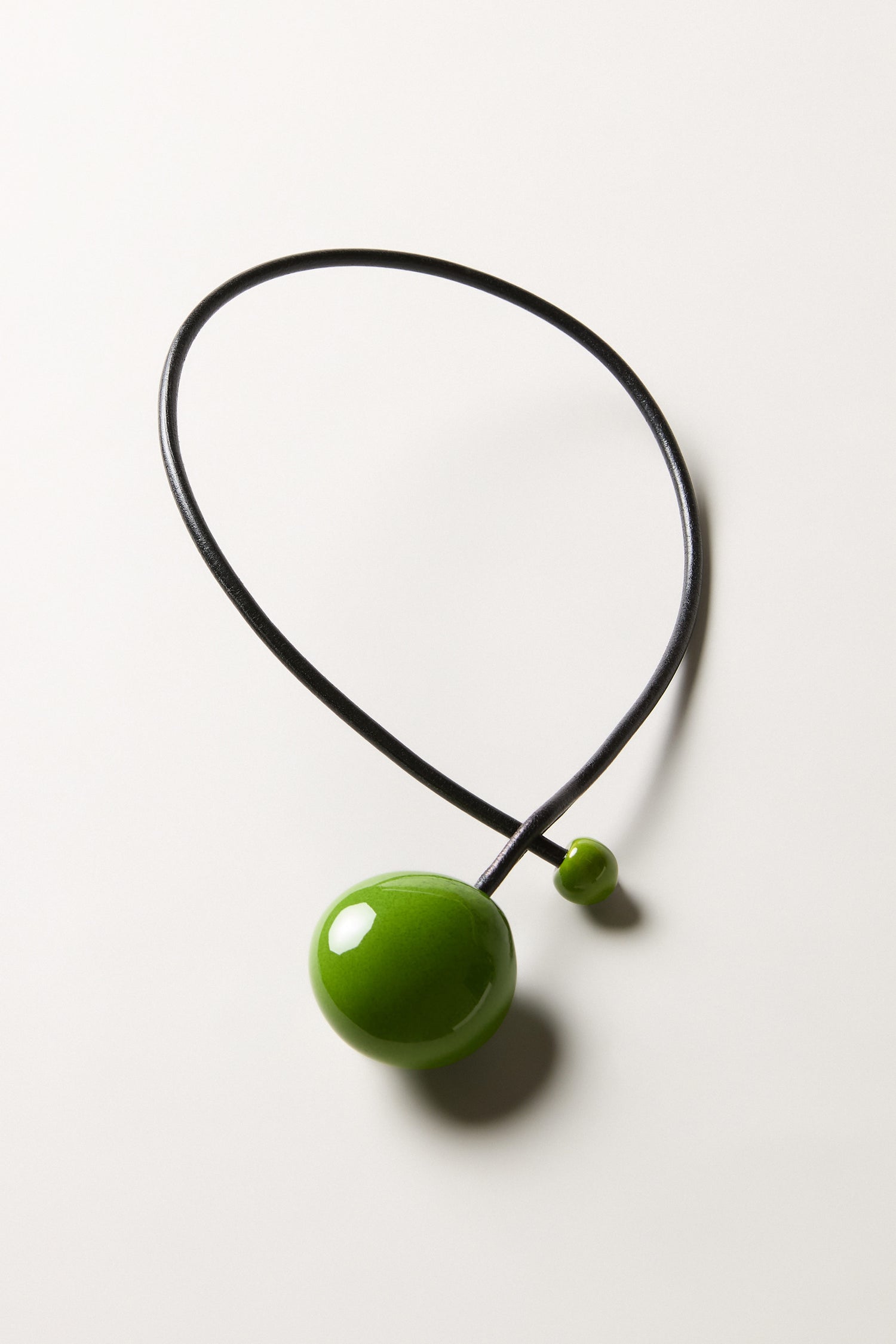 The Moss Handmade Ceramic Bead Necklace features a black choker with a large glossy green bead and a smaller green bead, reflecting elegant French design, shown against a plain white background.