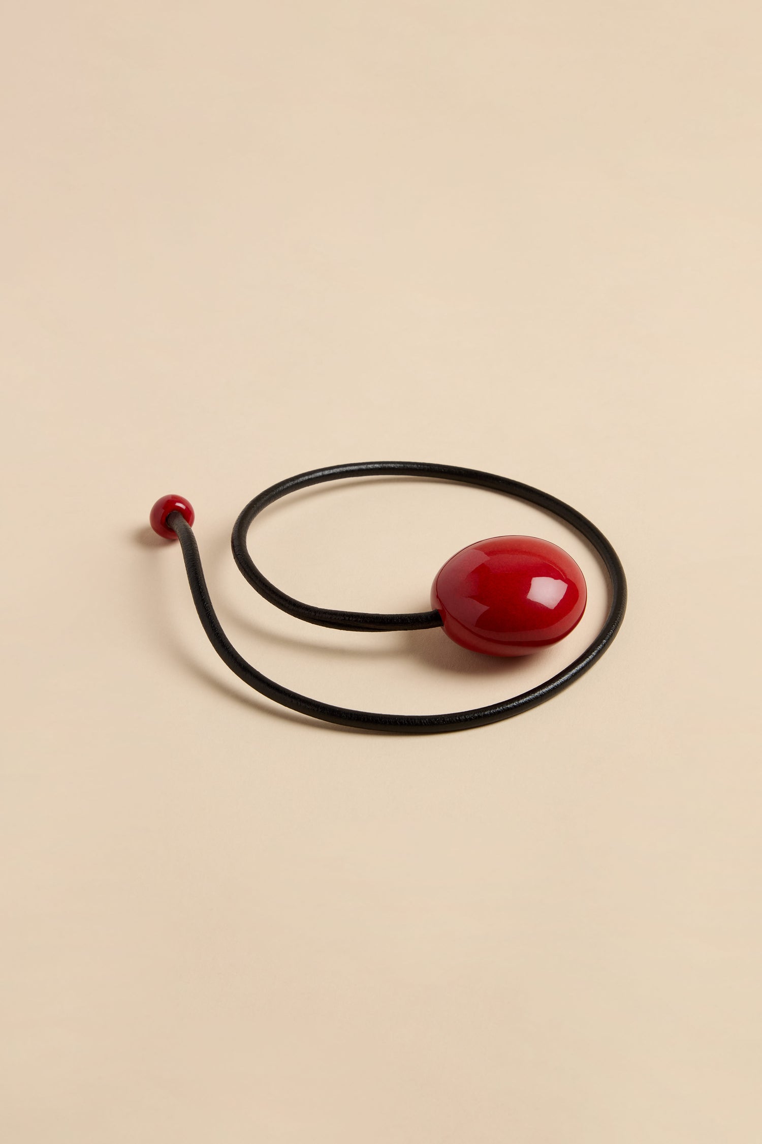 Handmade Deep Red Ceramic Bead Necklace featuring a black leather cord, a large smooth deep red ceramic bead, and a small matching bead at the end.