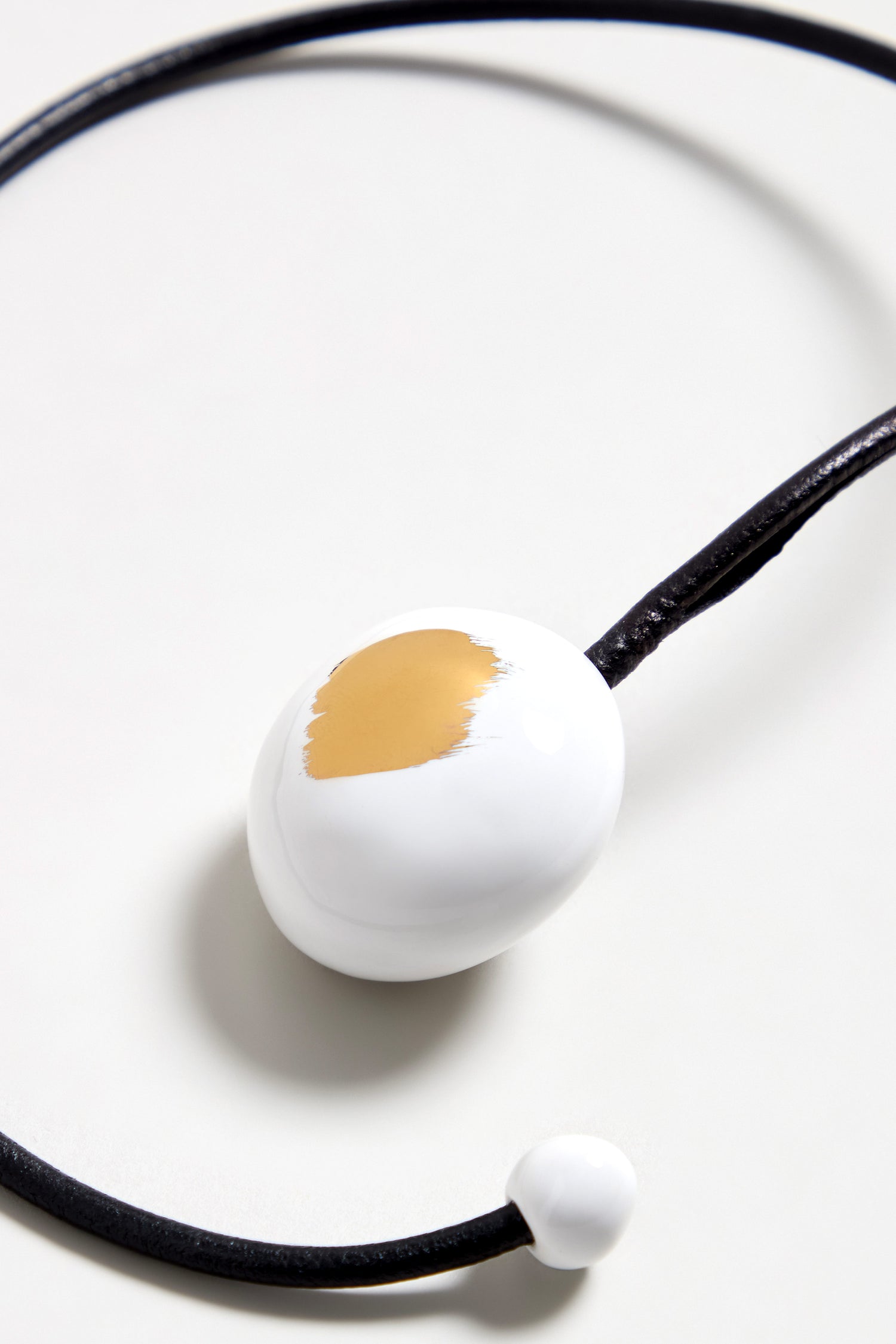 A handmade necklace featuring a white ceramic bead with gold brushstroke finish, inspired by French jewelry.