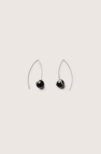 A pair of handmade ceramic graphic earrings featuring a modern minimalist teardrop shape with black stones and thin, curved wire hooks against a plain background.