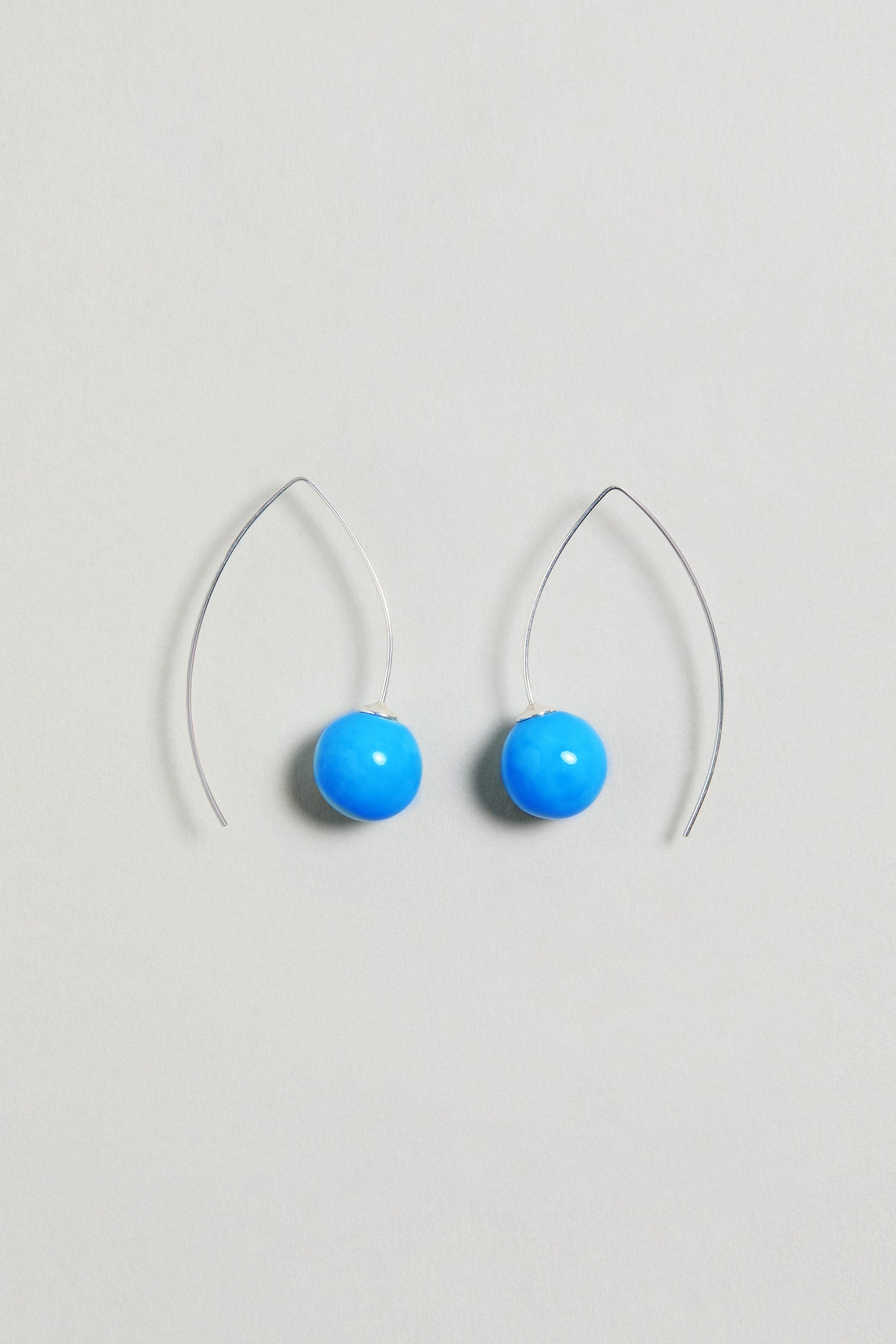 Handmade Ceramic Bead Earrings with silver hooks feature round, bright turquoise ceramic beads and are displayed on a light gray background. These earrings add a vibrant touch to any outfit.