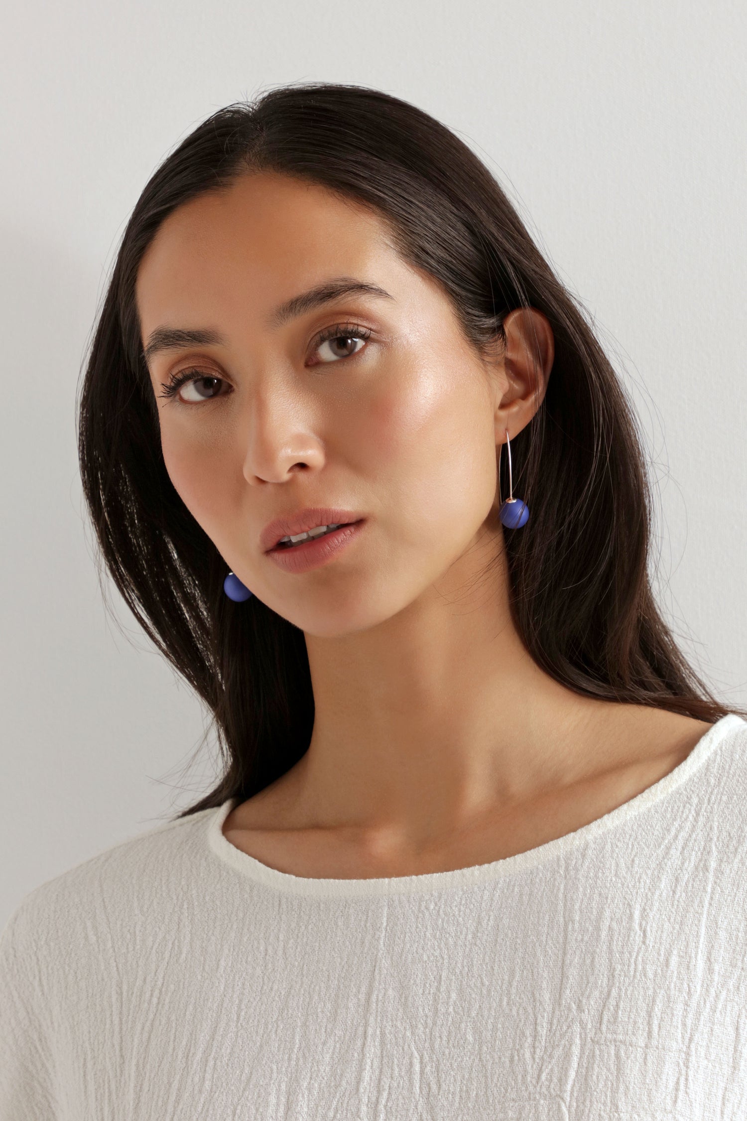Woman with long dark hair wears a textured white top and Handmade Ceramic Bead Earrings, featuring a sculptural twist design, as she looks at the camera against a plain light background.