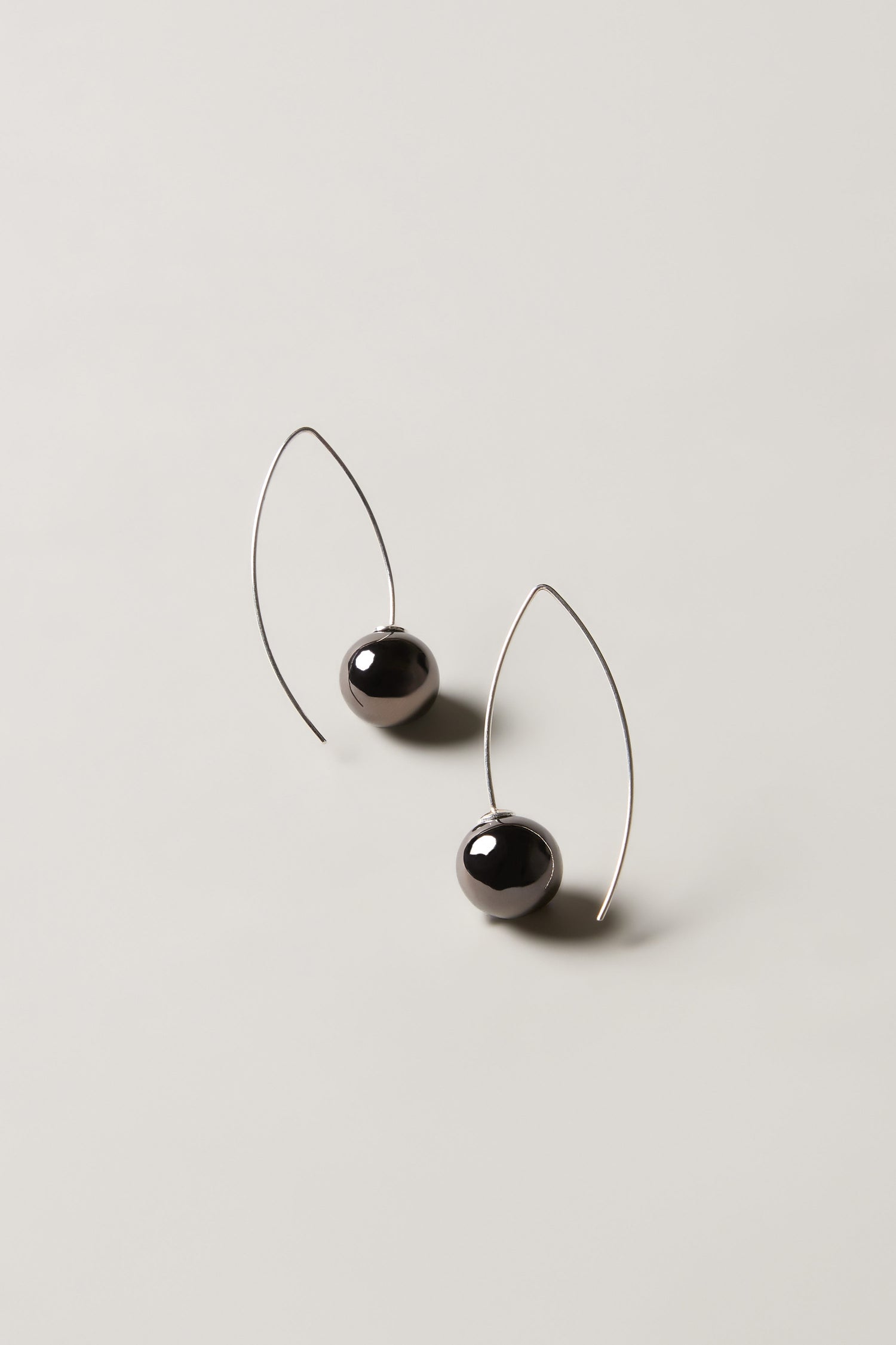 Handmade Ceramic Graphic Metal Earrings with thin, curved metal wires and round black beads, shown on a neutral background.