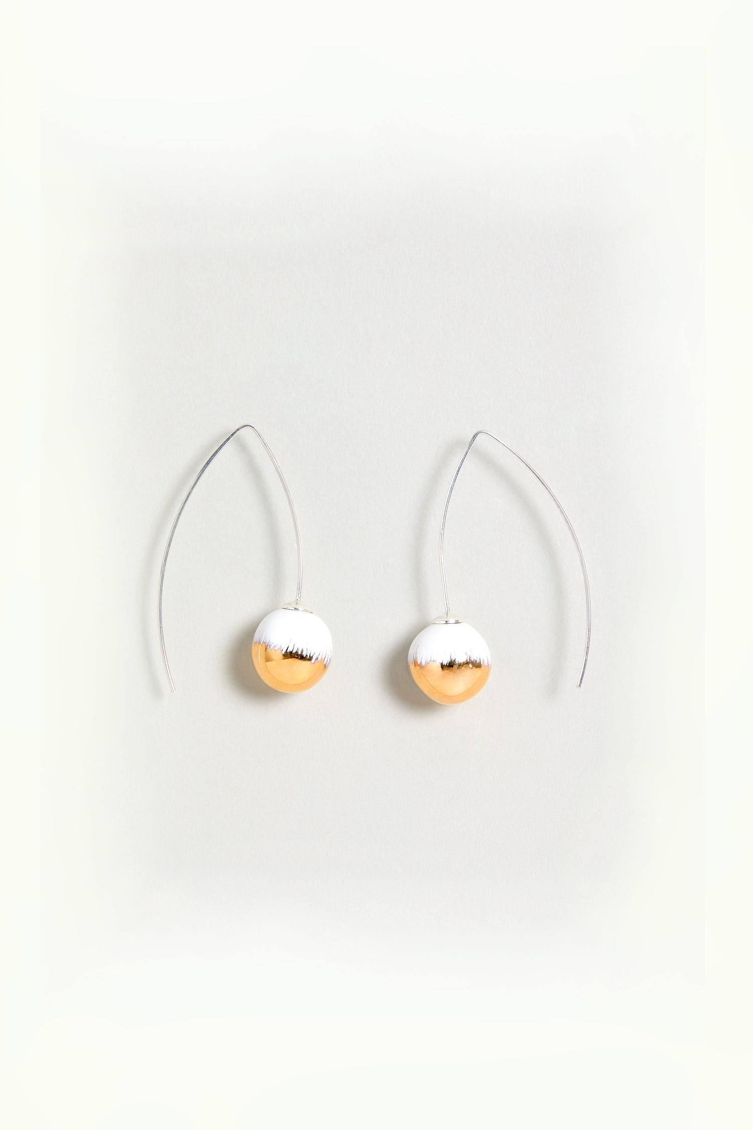 Handmade Gold Brushstroke Ceramic Bead Earrings featuring dangling gold and silver accents with thin curved wires and oval-shaped ceramic beads, displayed on a plain white background.