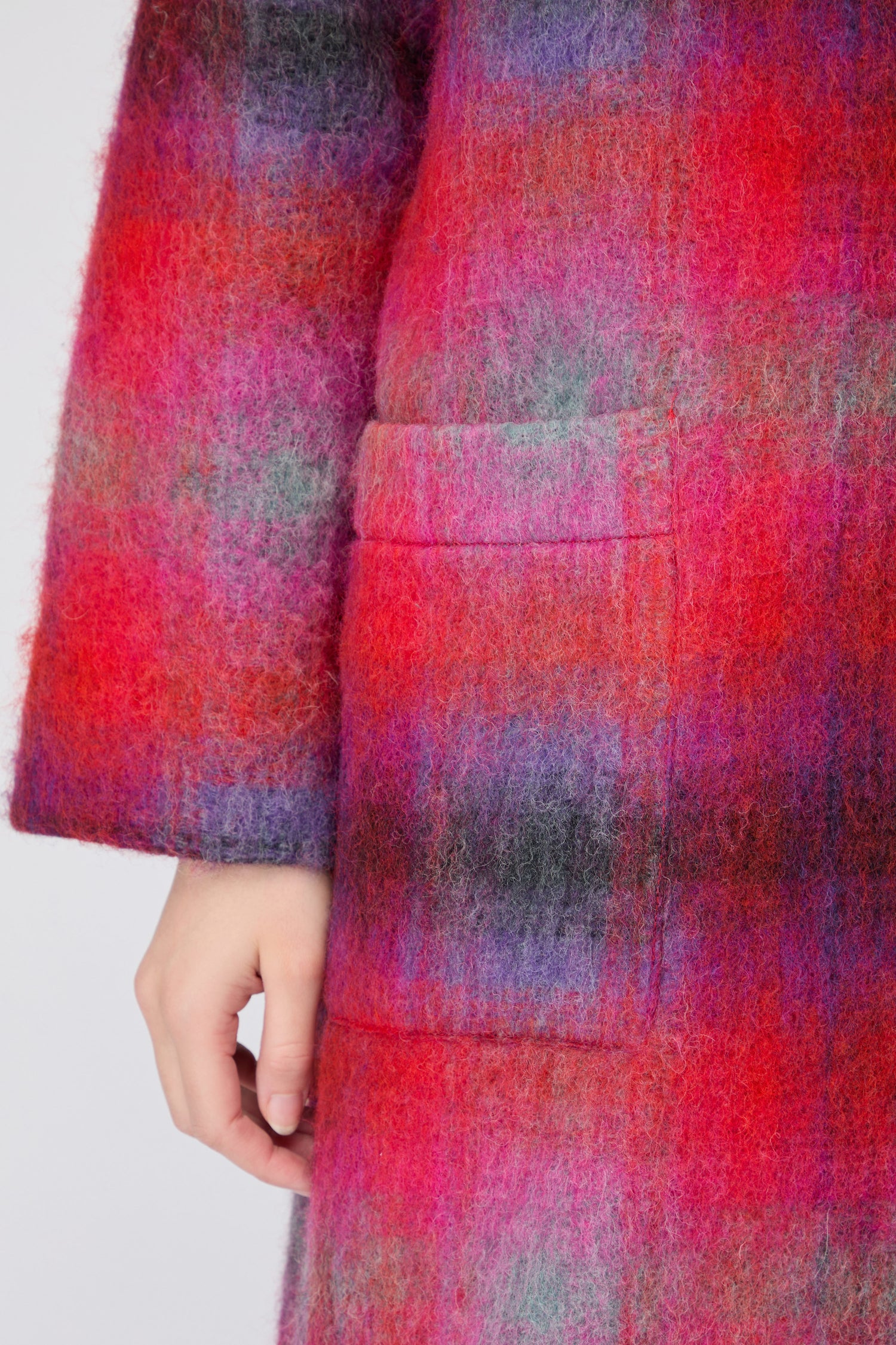 A woman wears the Bright Brushed Check Wool Coat—an oversized wool coat in red, purple, and black checks—styled with blue jeans and black boots against a plain background.