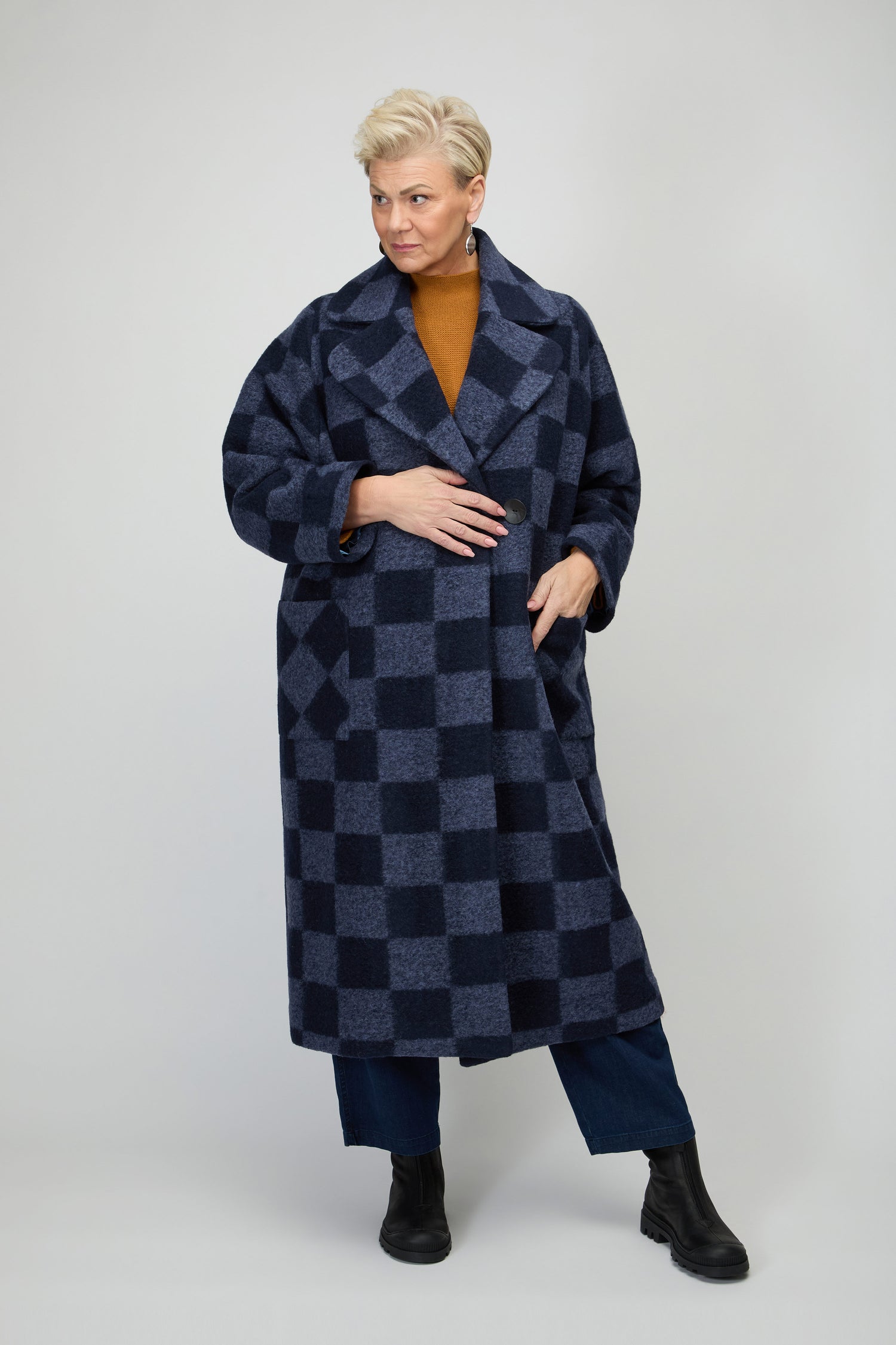 A person wearing the Checkerboard Wool Coat in dark blue over a brown top, blue pants, and black boots stands against a plain light background.