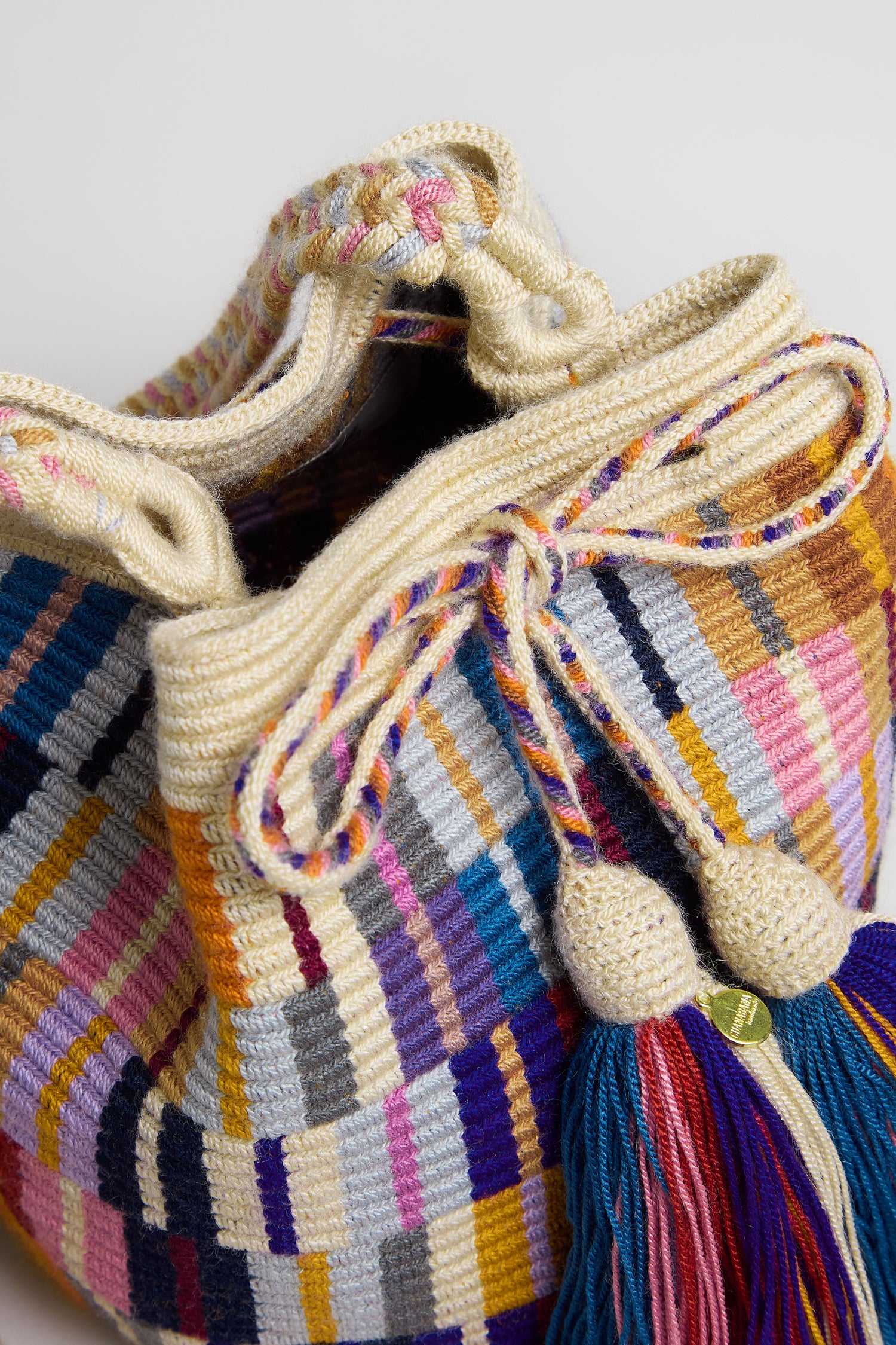 The Hand Crocheted Wayuu Crossbody Bag showcases multicoloured stripes, a braided drawstring closure, and two large tassels at the front.