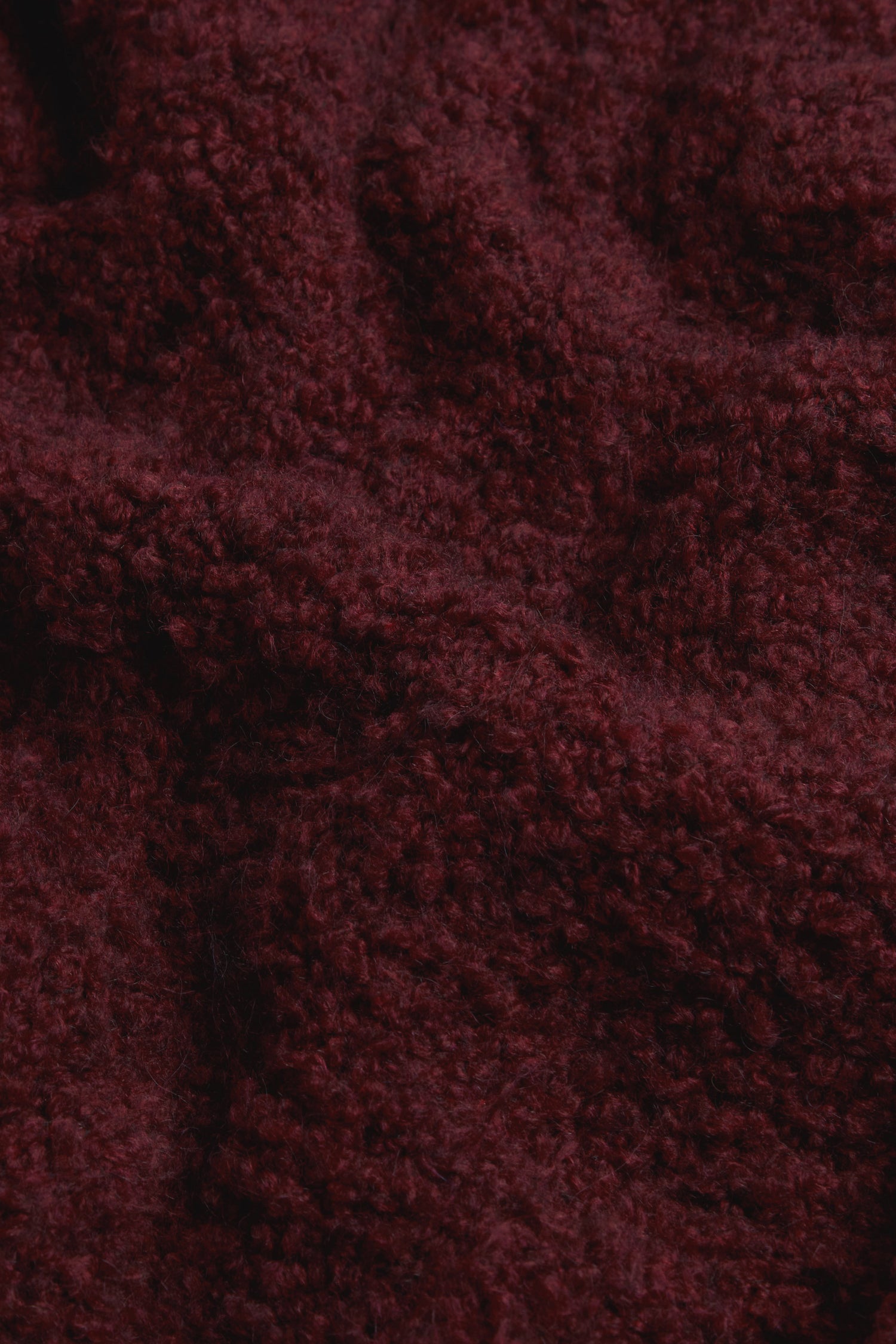 Close-up of the Bordeaux Boucle Cable Knit Jumper, showcasing its textured, dark burgundy fabric with a soft and fuzzy surface reminiscent of classic winter knits.