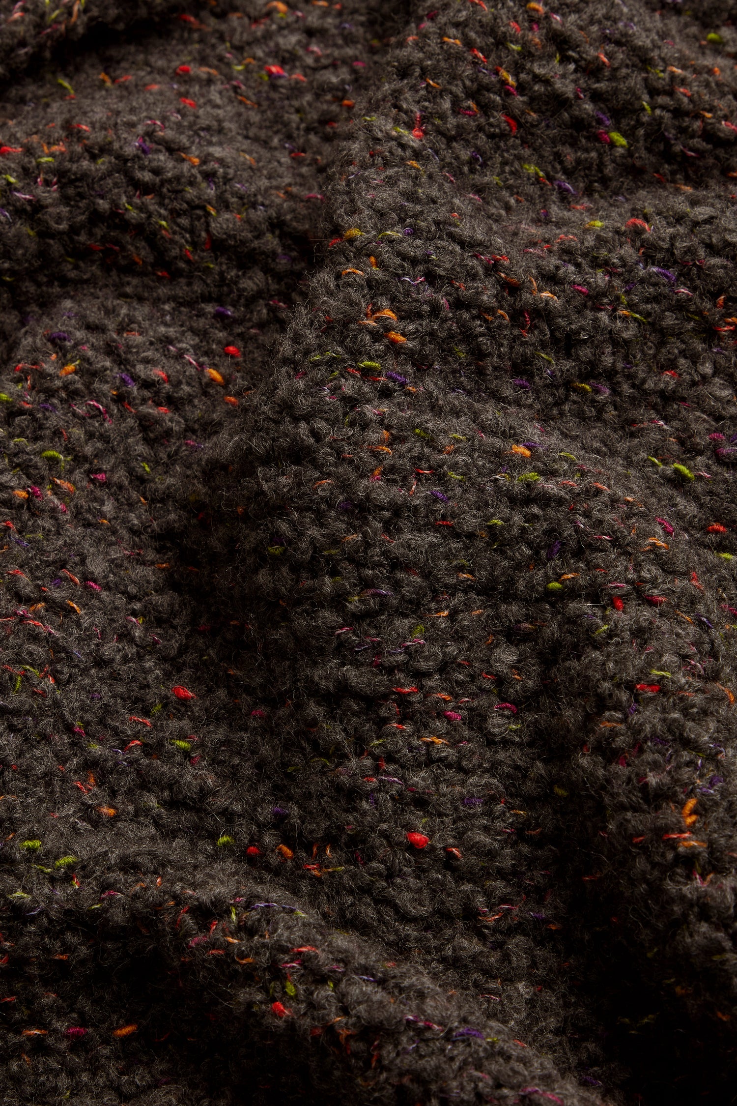 Close-up of the Graphite Boucle Cable Knit Jumper, featuring dark textured wool fabric with multicolored flecks and a distinct knit pattern, highlighting folds and detailed surface textures.
