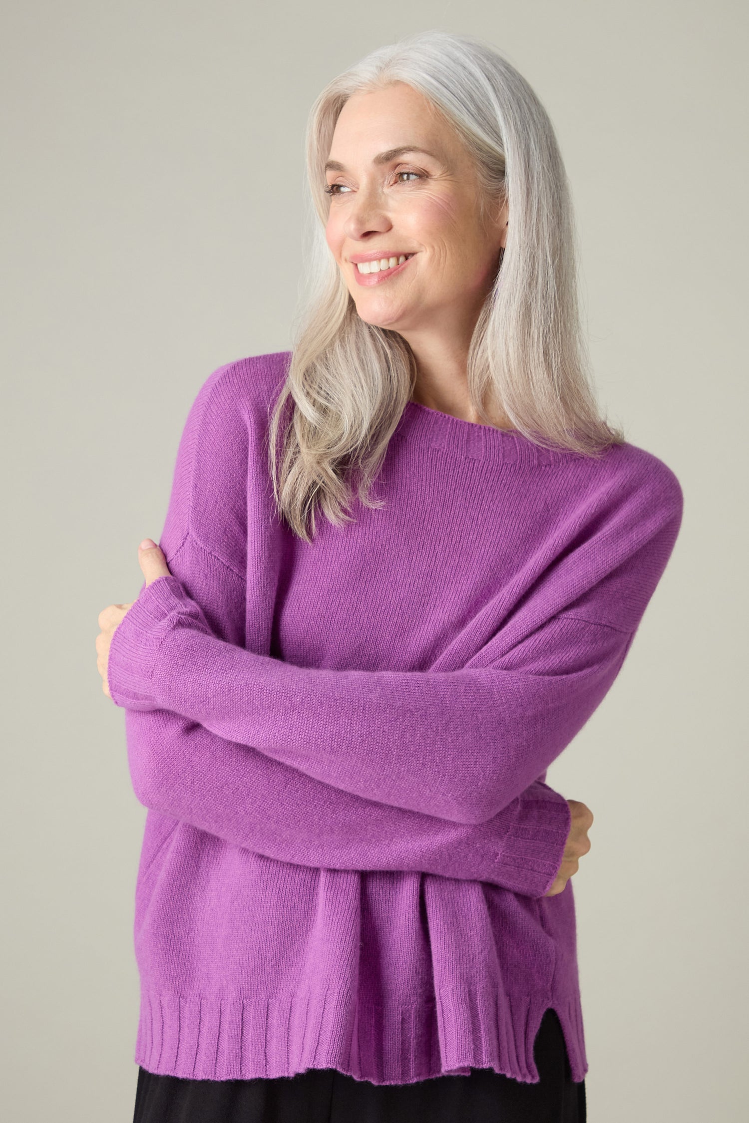A person with long gray hair smiles while wearing the luxurious Merino Wool Crop Jumper in purple, exuding comfort against a neutral background.