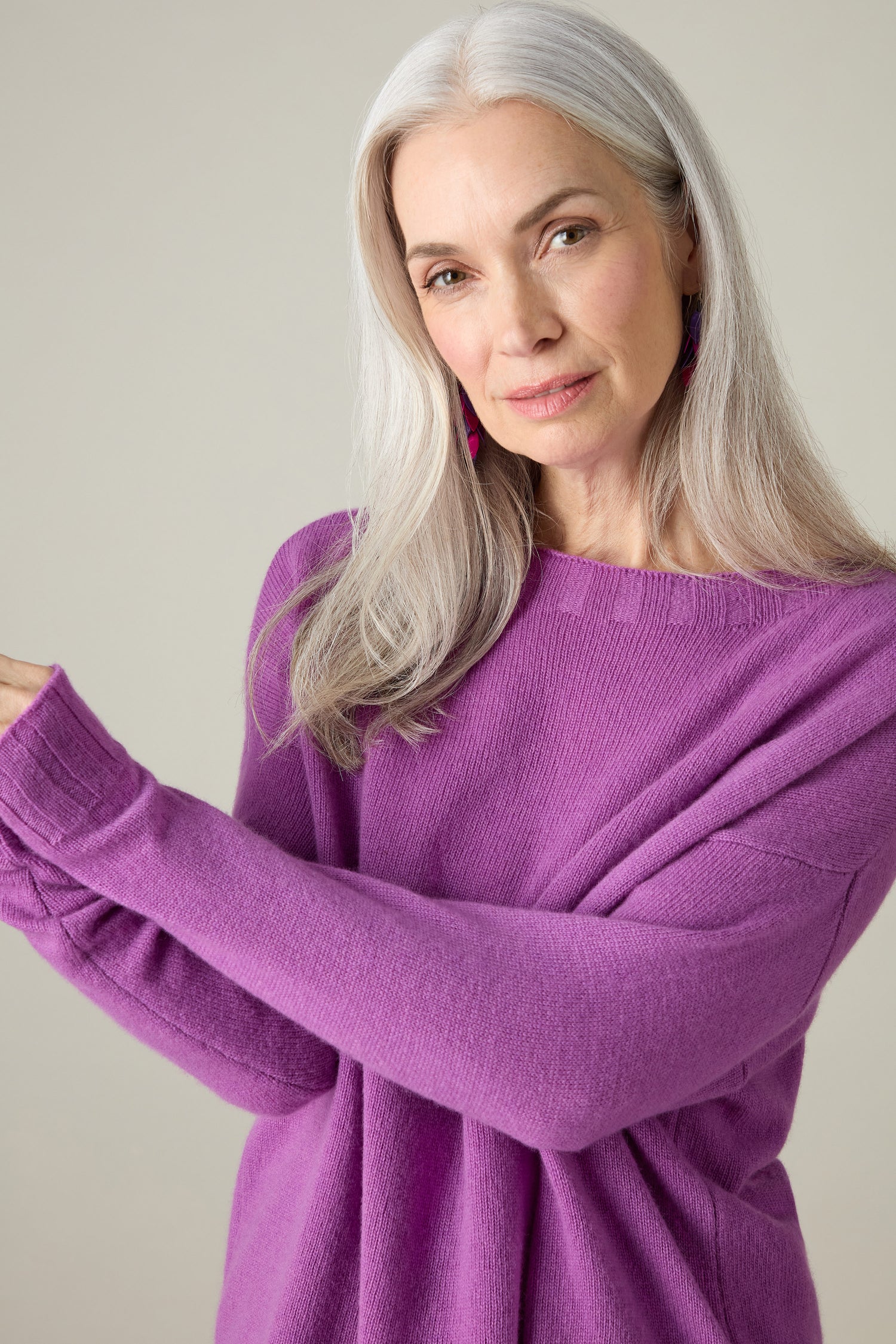 A woman with long gray hair models the exquisite Merino Wool Crop Jumper in a deep purple shade, posing elegantly against a neutral background.