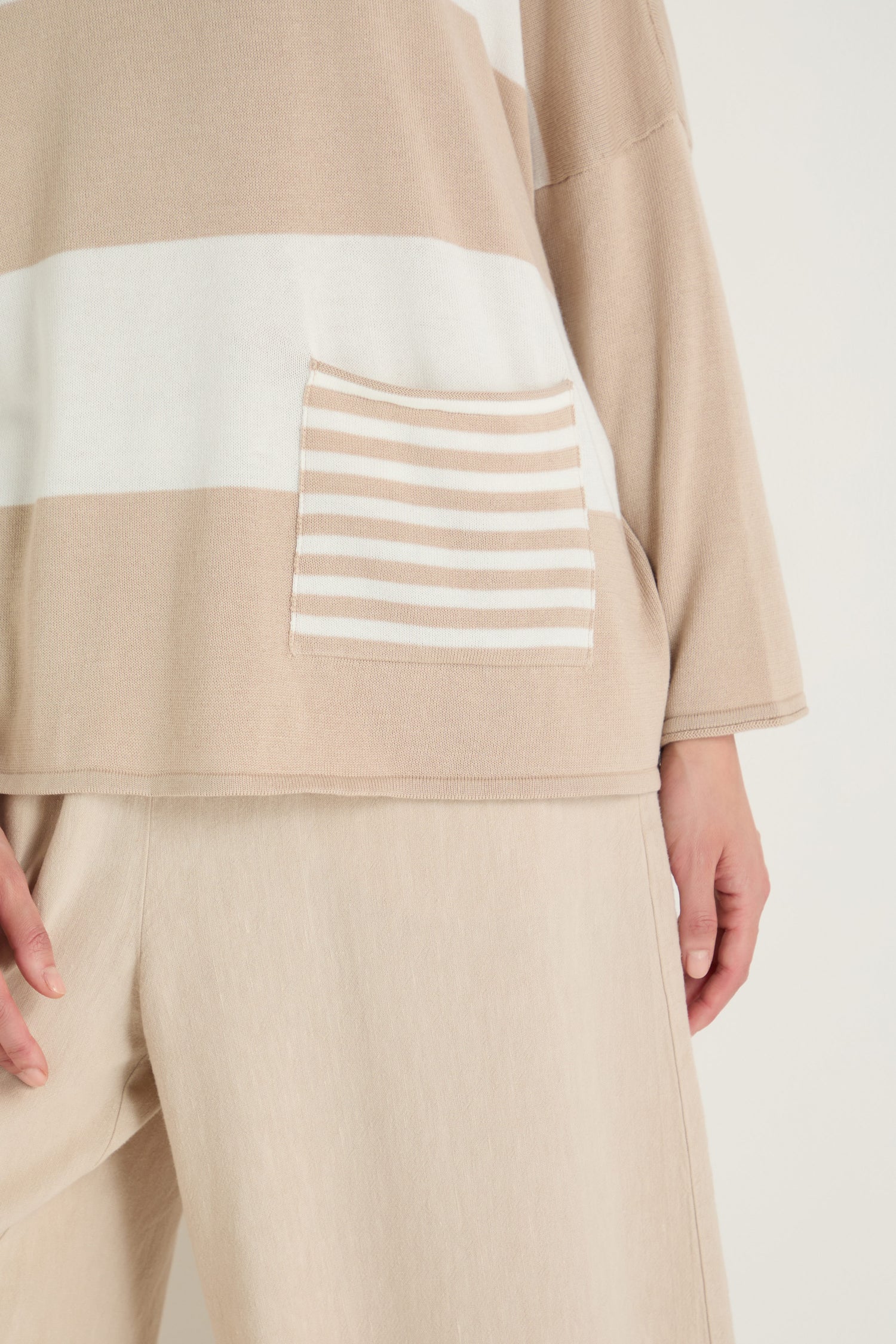 Wearing the Stripe Pocket Knit Top in beige-and-white stripes, featuring a striped pocket and crafted from modal cotton in a relaxed, boxy shape, paired with beige wide-leg pants.