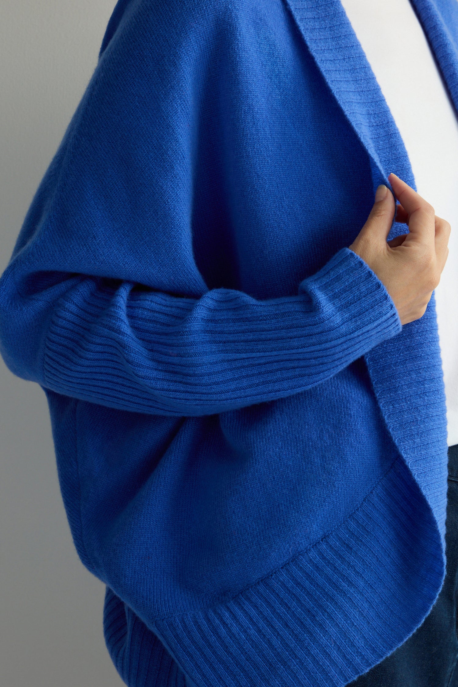 A person wears the Merino Ribbed Cuff Shawl Cardigan in blue over a white shirt, highlighting the sophistication of our Knitwear Collection.