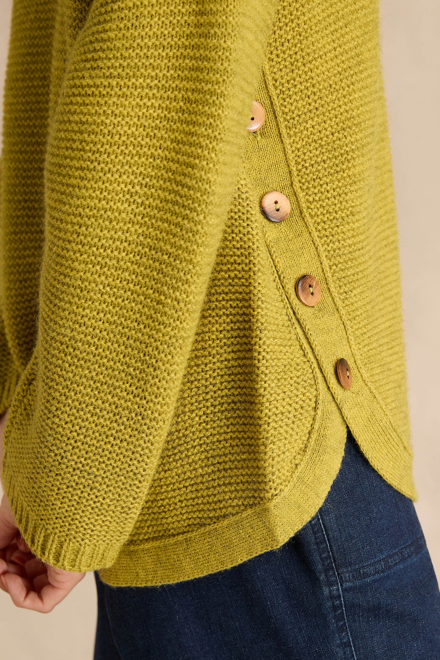 Person wearing the Avocado Ribbed Wool Blend Button Jumper, a textured yellow-green sweater with side button detail, paired with blue denim jeans.