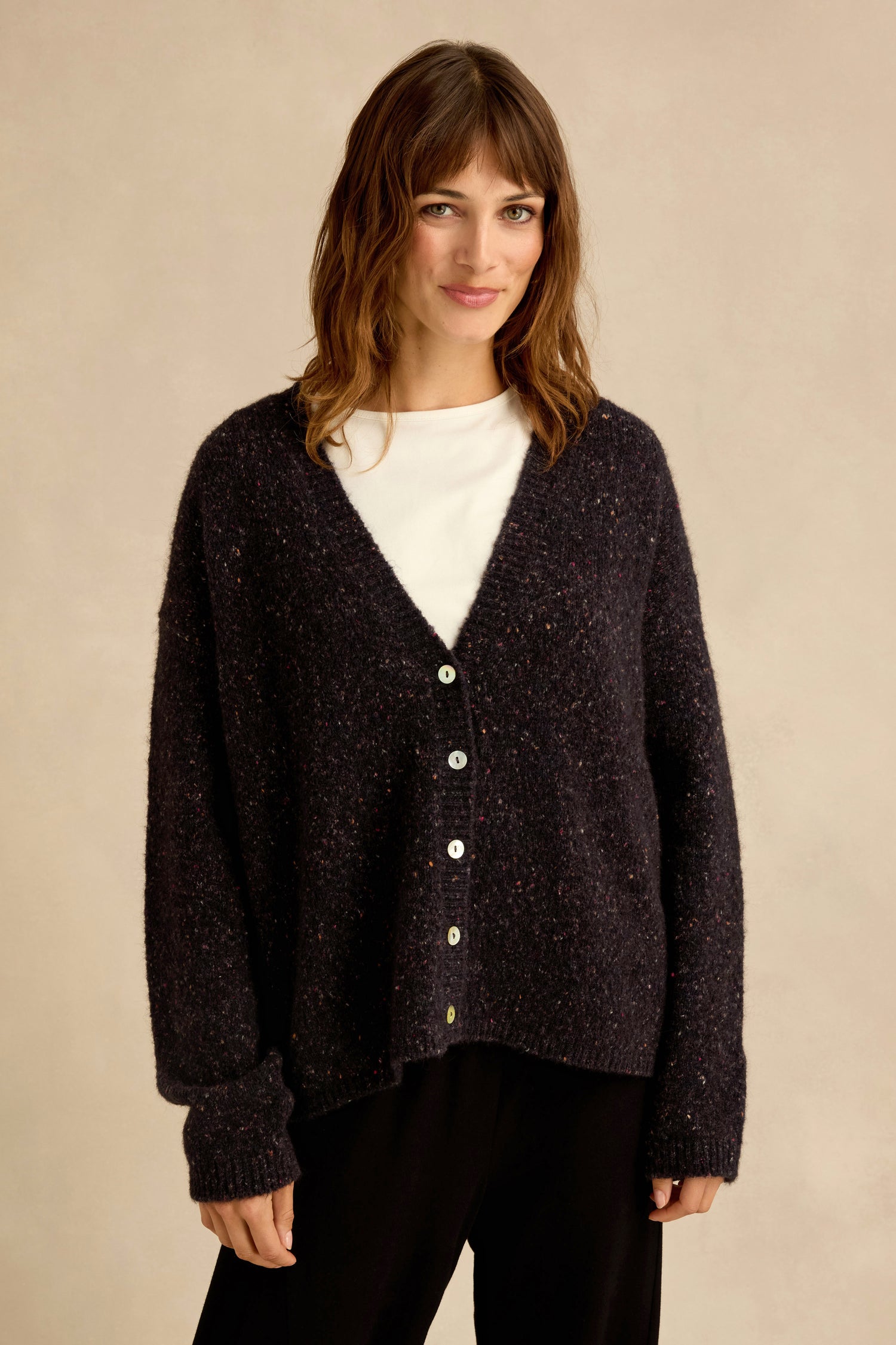 A woman with wavy brown hair wears the Night Alpaca Blend Cropped Cardi over a white shirt and black pants, standing against a plain beige background.