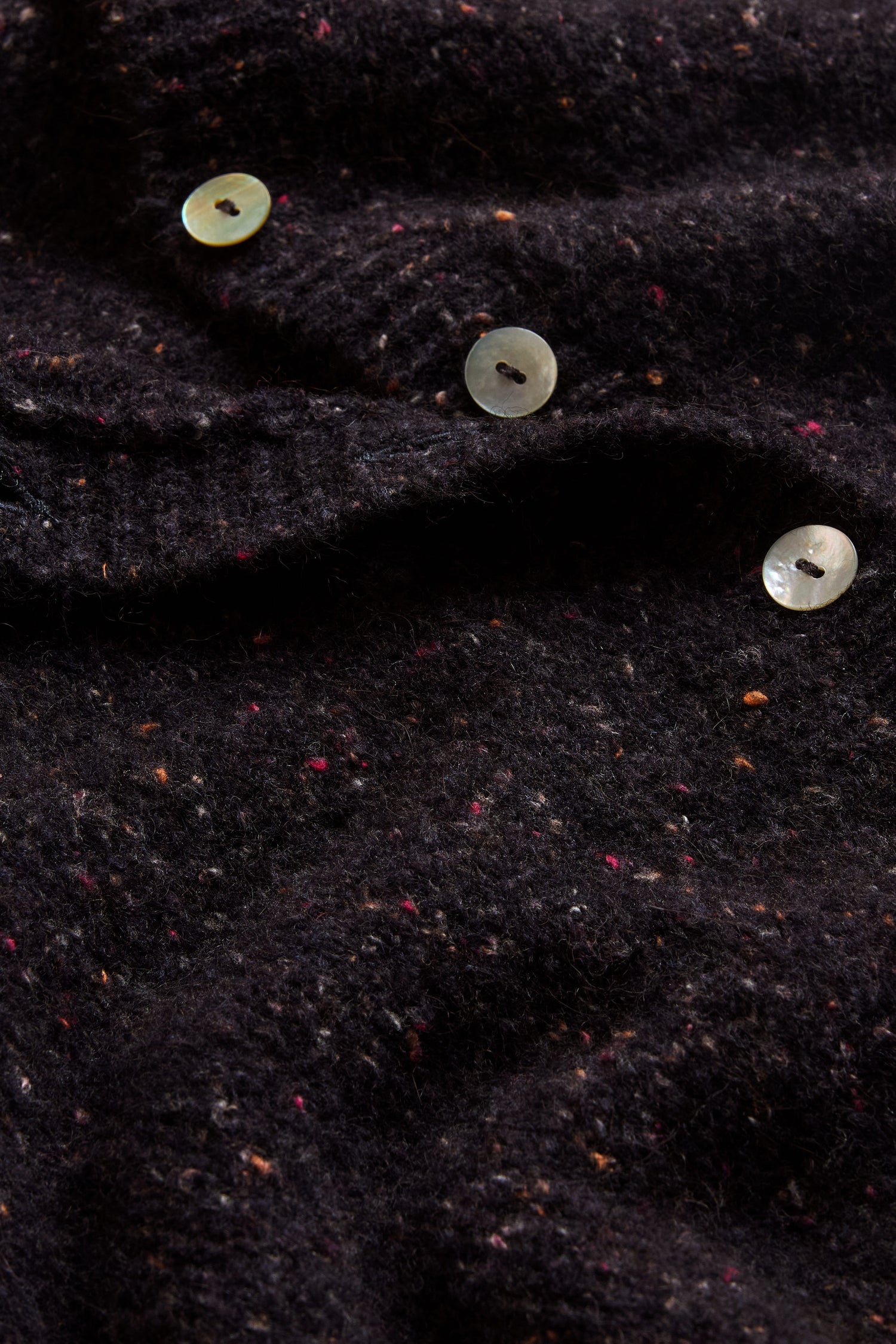 Close-up of the Night Alpaca Blend Cropped Cardi—a dark, textured alpaca blend cardigan featuring three light-colored buttons and subtle colored flecks throughout the fabric, highlighting the refined details of Italian knit craftsmanship.