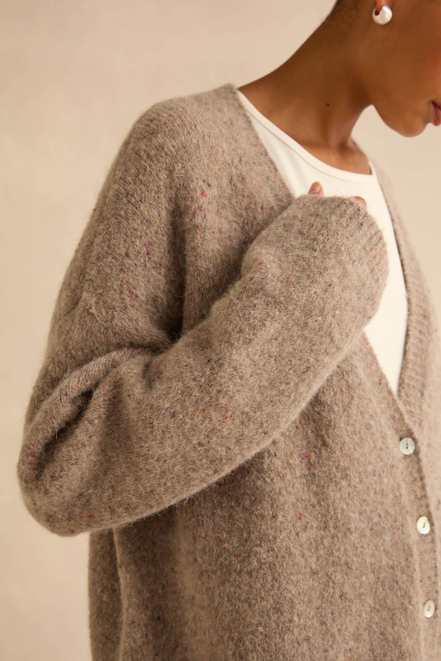 A person wearing an open, taupe-colored Taupe Alpaca Blend Cropped Cardi with subtle multi-colored flecks.