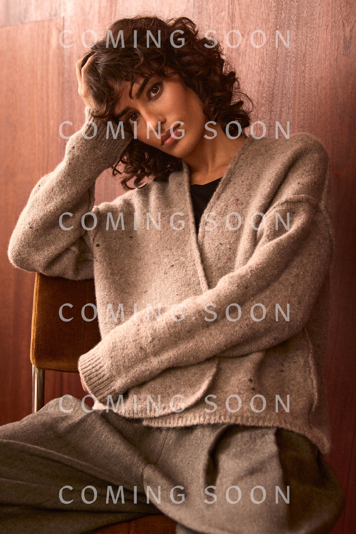 A person with curly hair sits on a chair, wearing the Taupe Alpaca Blend Cropped Cardi and matching pants. The words “COMING SOON” and “GOK6995-CON” are overlaid on the image multiple times.