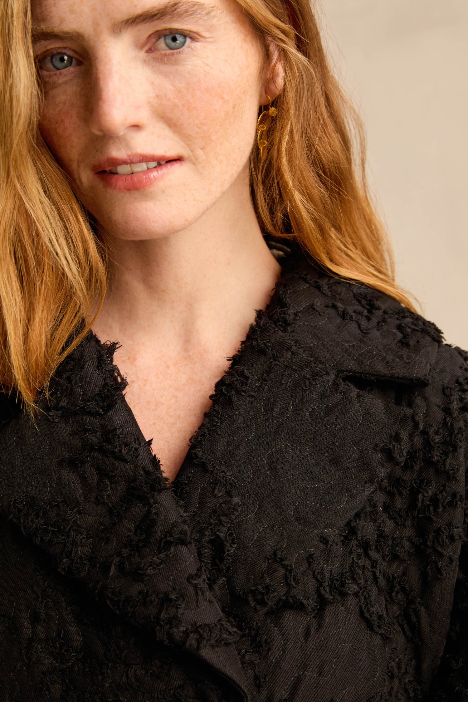A woman with long red hair wears the Textural Big Collar Coat and gold earrings, gazing slightly past the camera against a neutral background.