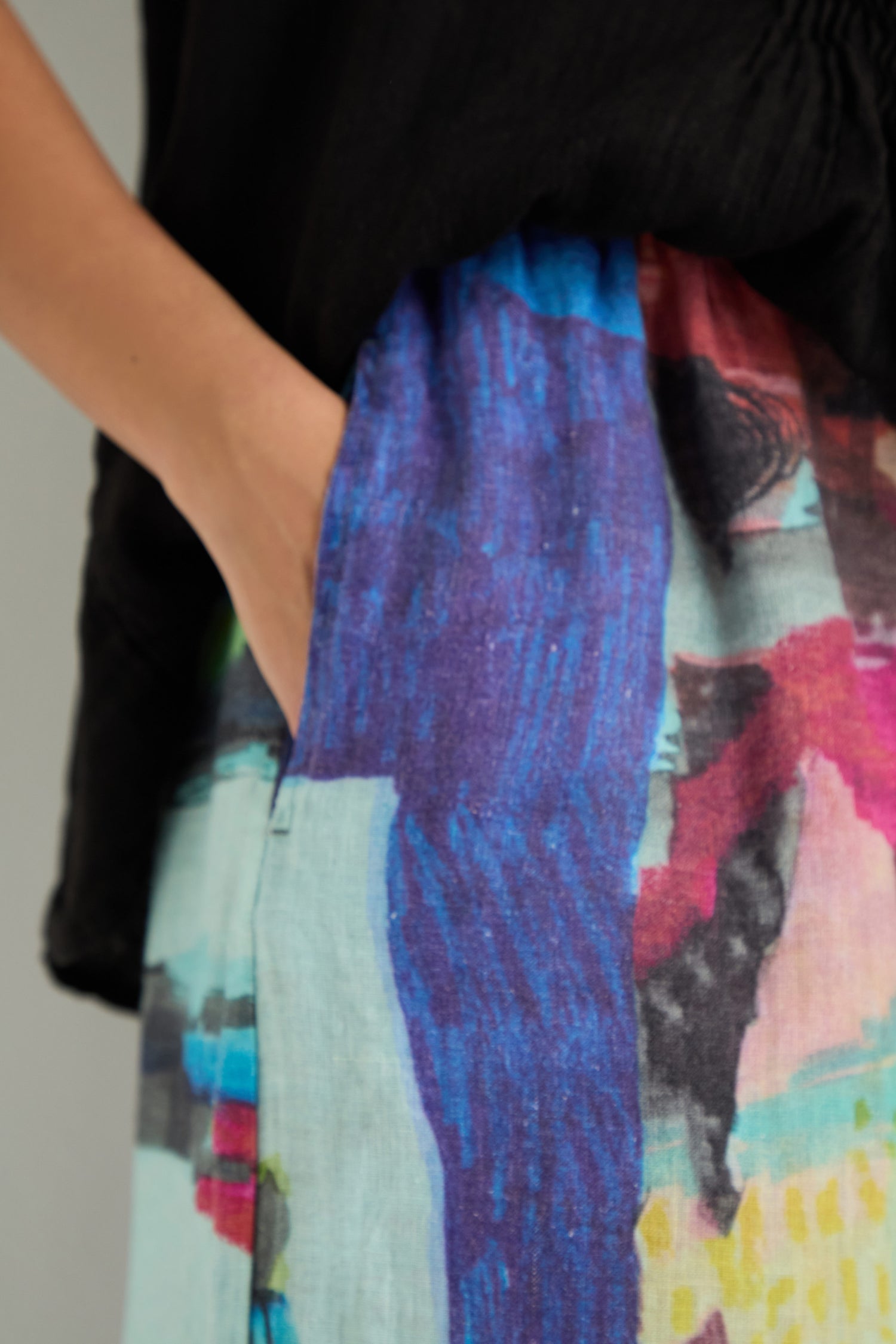 Close-up of a person in a black top and vibrant Abstract Print Wide Leg Trousers, with their left hand tucked into the pocket.