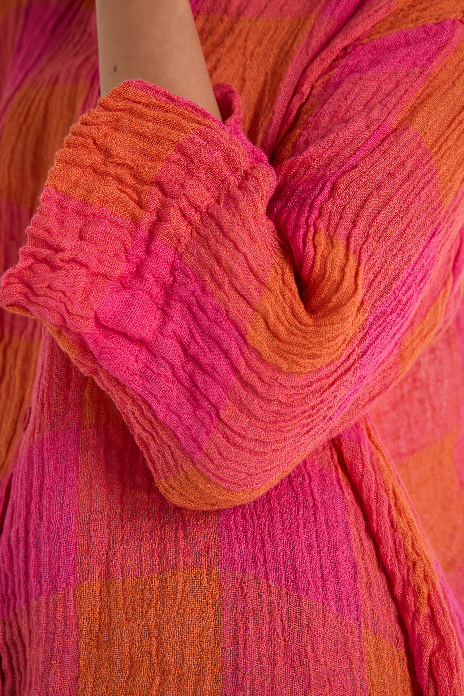 Close-up of a person’s arm bent at the elbow, wearing the Large Check Linen Swing Shirt featuring a pink and orange check pattern.