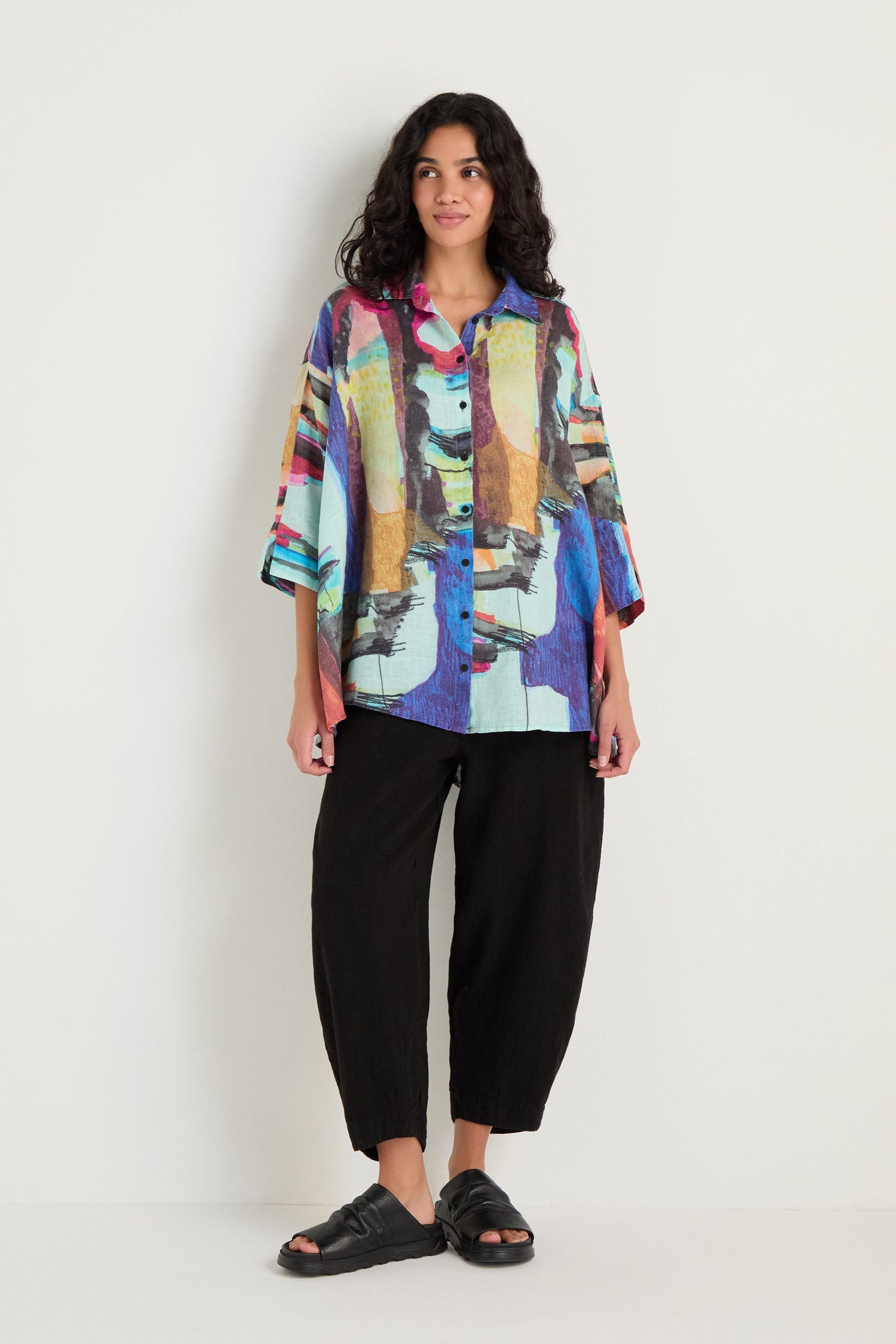 A person stands against a plain background wearing the Abstract Print Flared Shirt, paired with loose black pants and black sandals.
