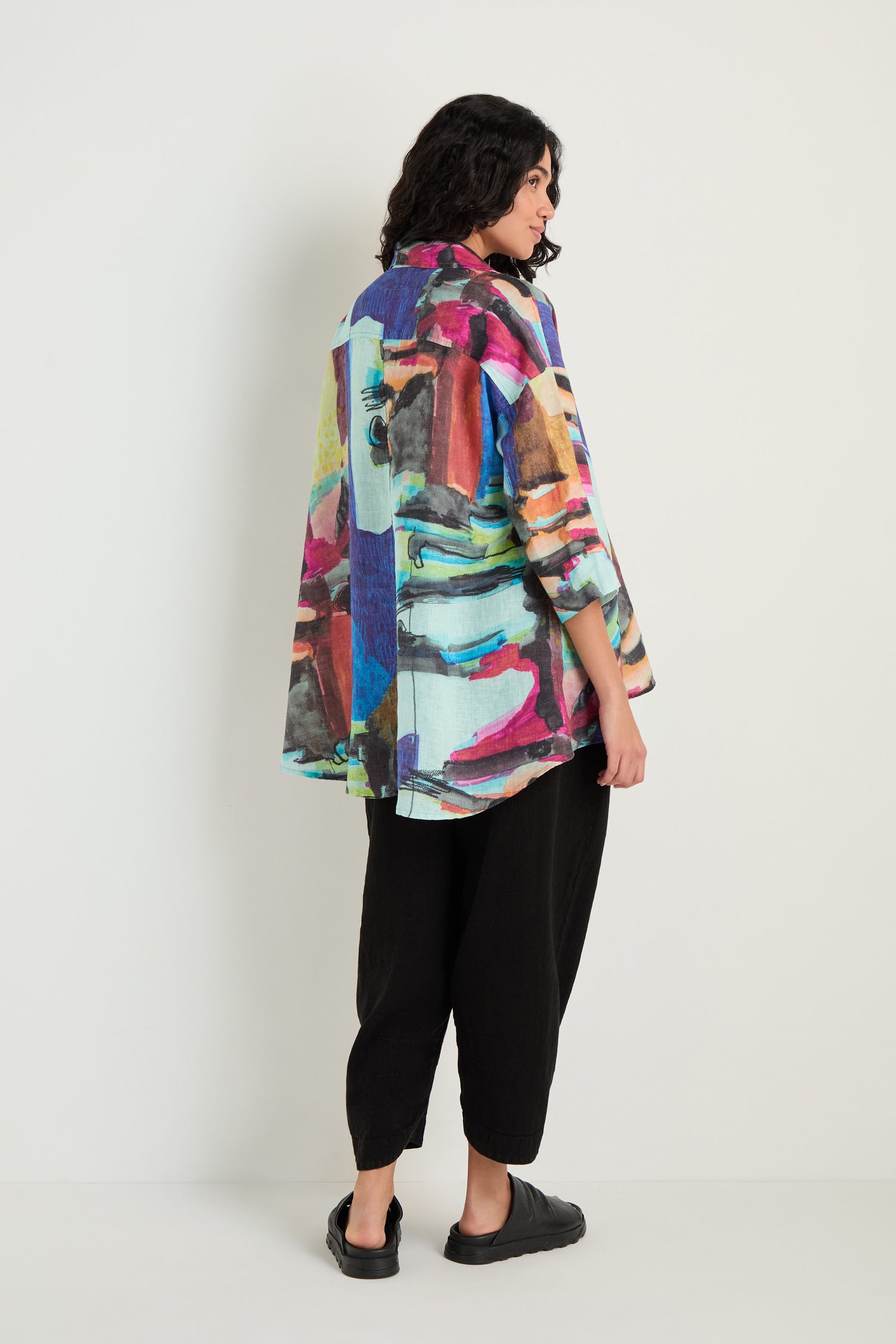 A person stands sideways in an Abstract Print Flared Shirt, paired with black pants and shoes against a plain light background—the breathable linen fabric ensures relaxed comfort with bold style.