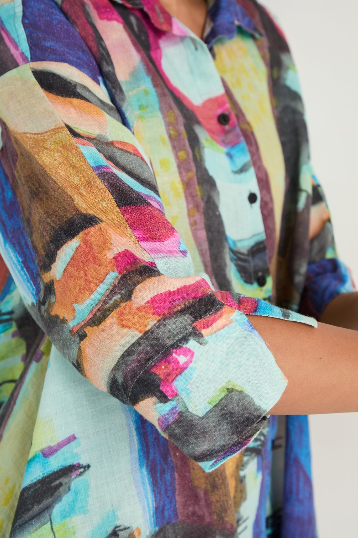 Model wears the Abstract Print Flared Shirt, made from breathable linen with a colorful abstract pattern in blue, pink, orange, yellow, and black. Only the torso and part of one arm are visible.