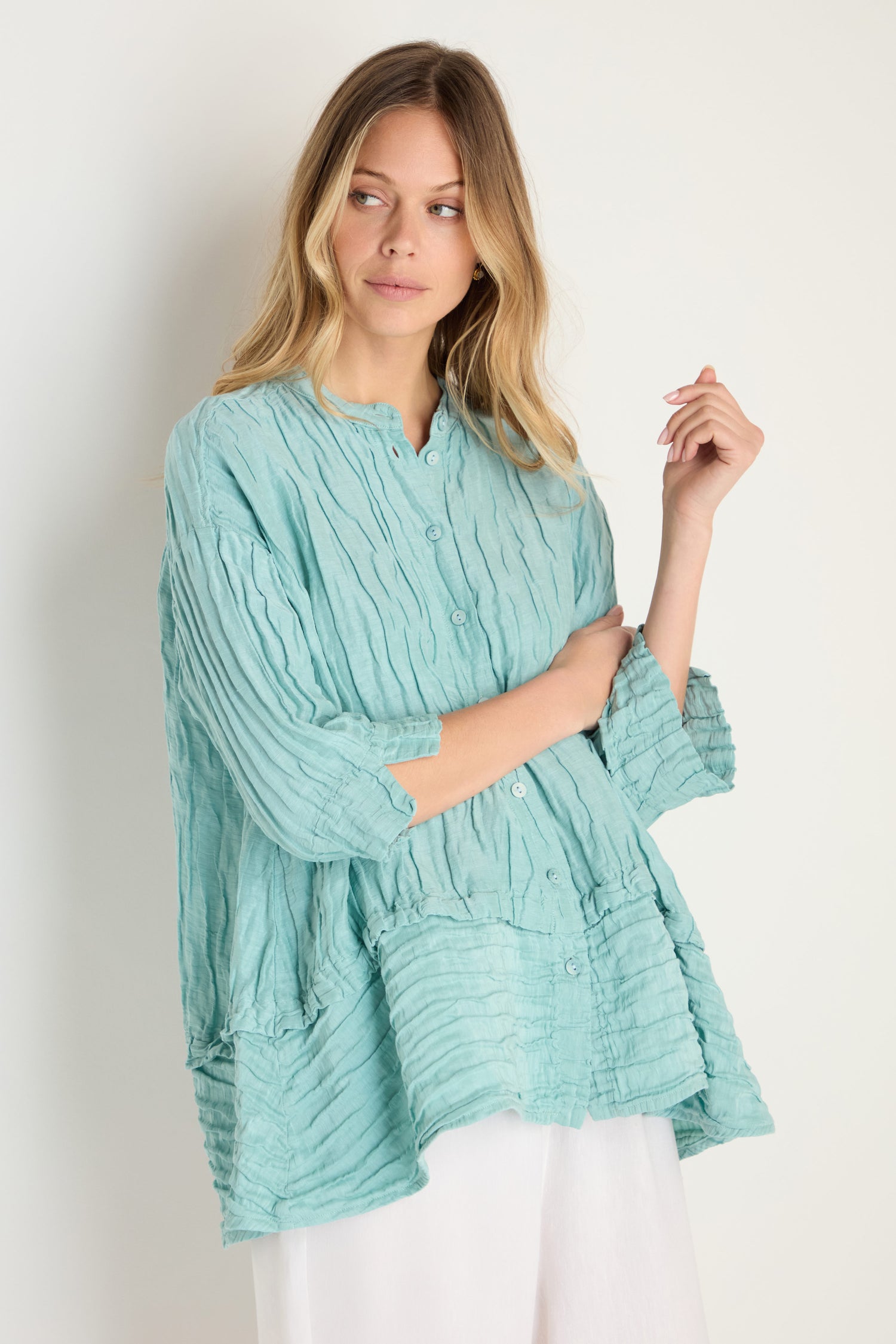 A woman wears the Panel Hem Silk Linen Shirt in light blue, featuring a breathable fabric, oversized fit, and three-quarter sleeves, paired with white pants against a plain light background.