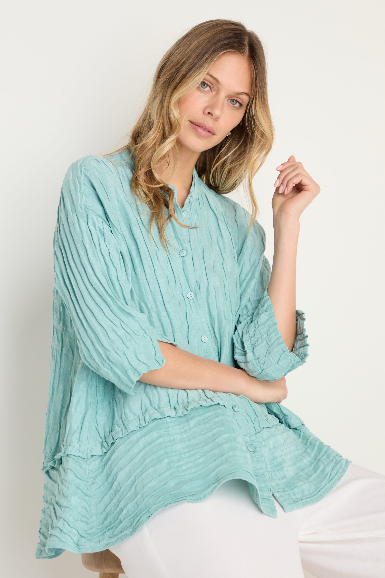 Woman in the Panel Hem Silk Linen Shirt, featuring a loose, breathable fit with buttons and an oversized style, paired with white pants against a plain light background.